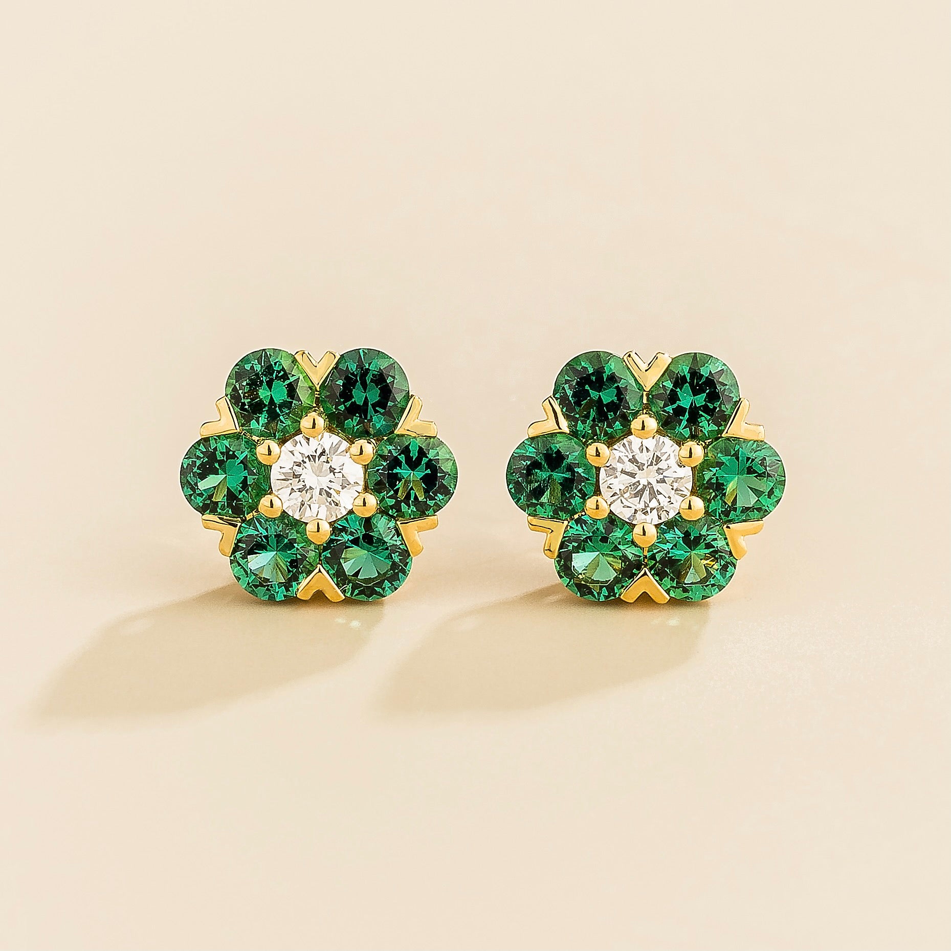A pair of gold earrings featuring a central diamond with emerald accents arranged in a floral daisy pattern.