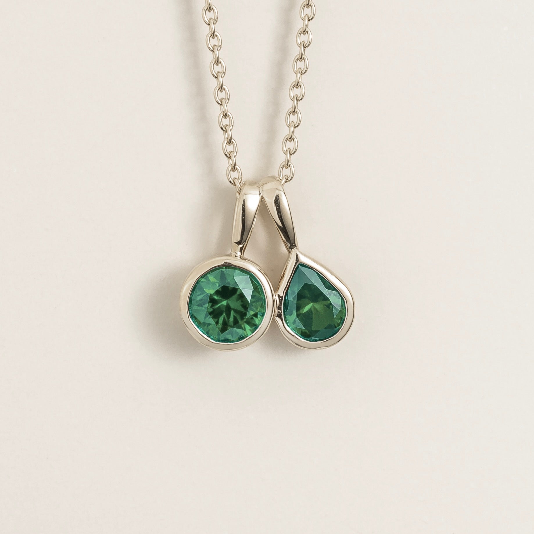 Juvetti white gold pendant necklace featuring a duo of round and pear-cut lab-grown green sapphires.