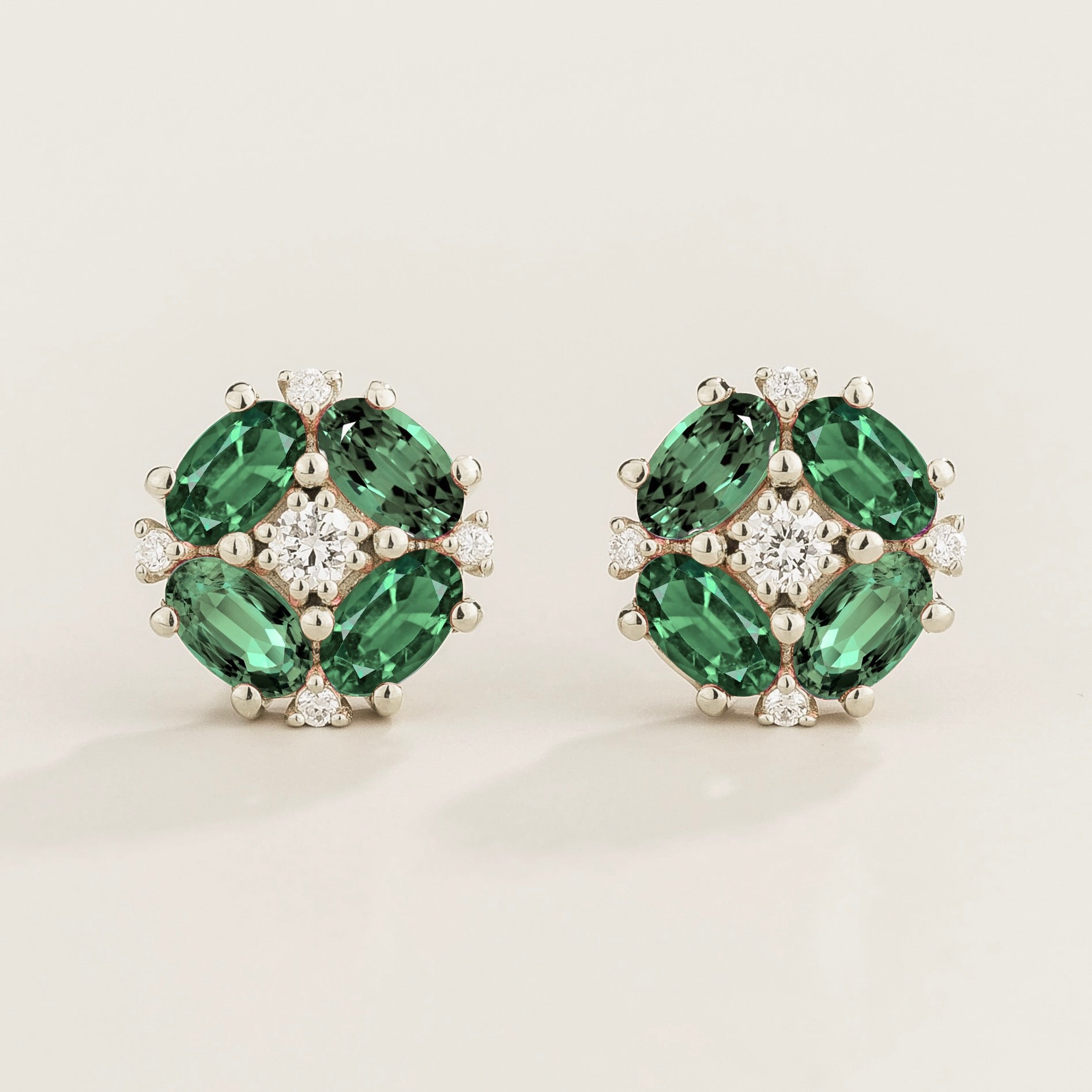 A pair of white gold earrings featuring oval emeralds and round surrounding diamonds.