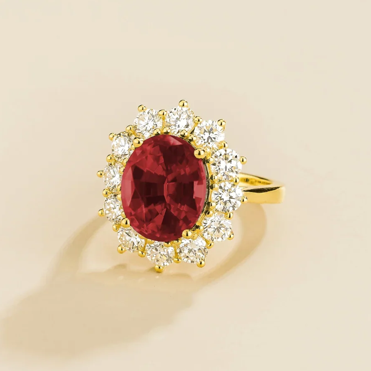 Gold ring with a large ruby gemstone and diamond halo accents on a beige background