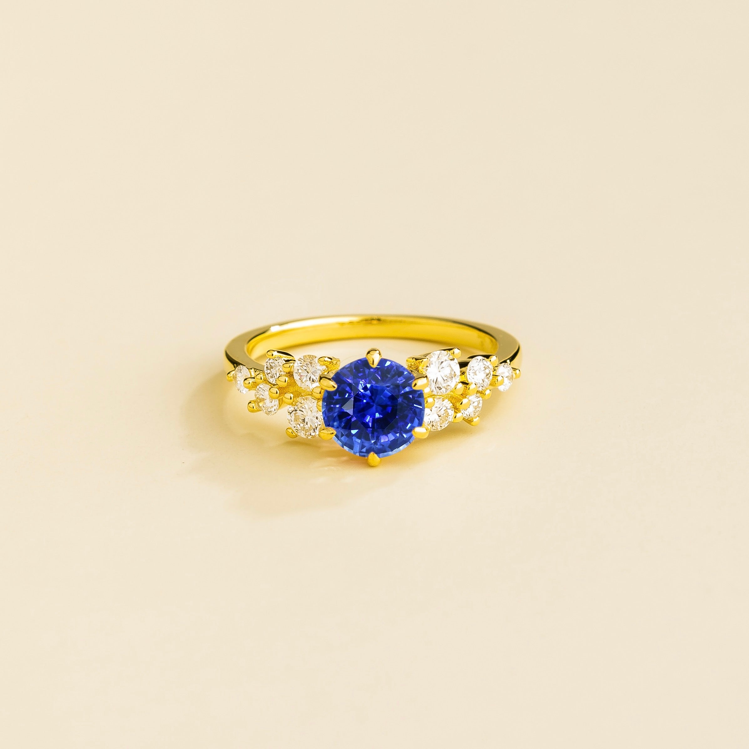 A gold ring with a blue sapphire center stone and smaller diamonds cluster set in gold, displayed against a neutral background.