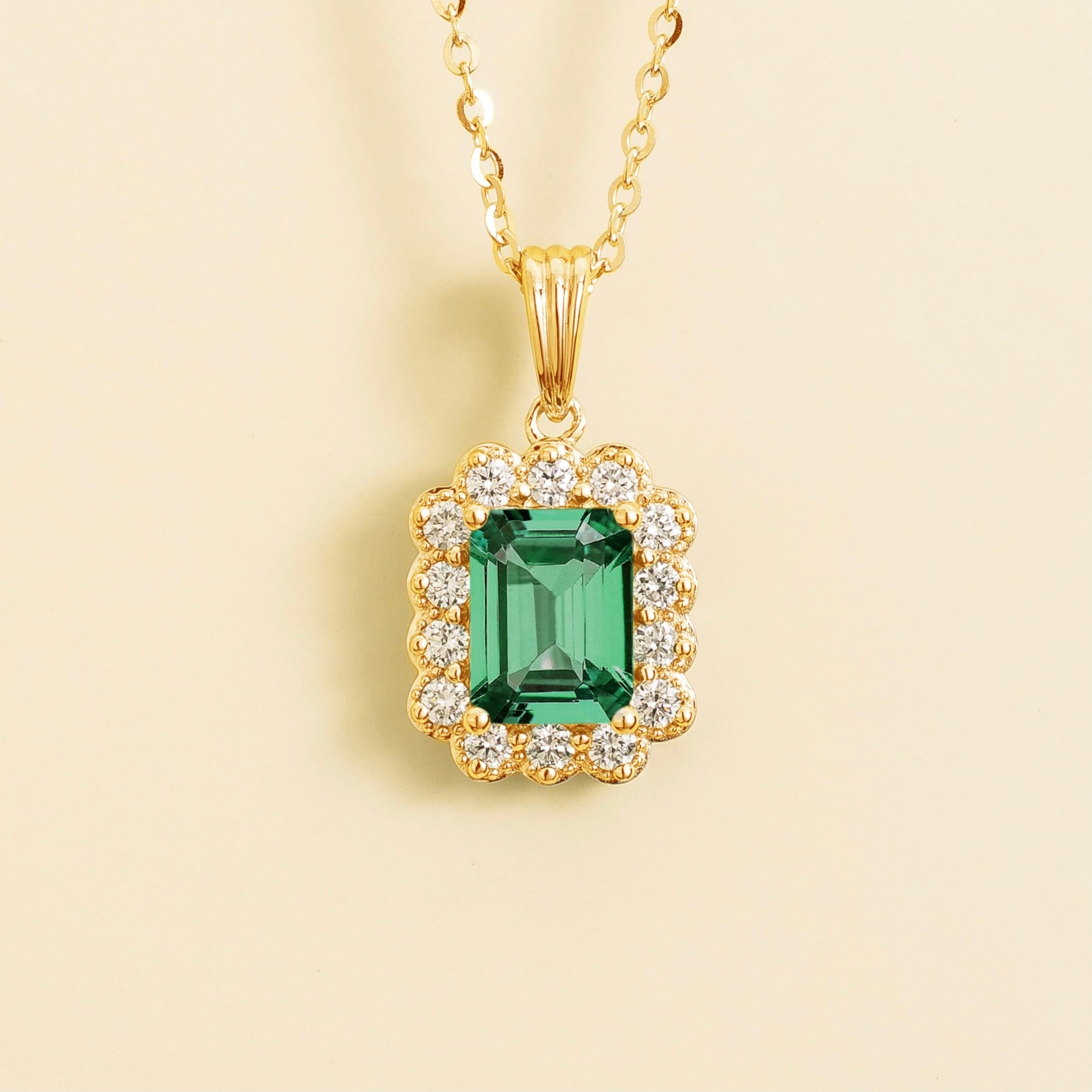 A gold necklace with an emerald cut emerald centerpiece surrounded by a halo of diamonds, displayed against a light background.