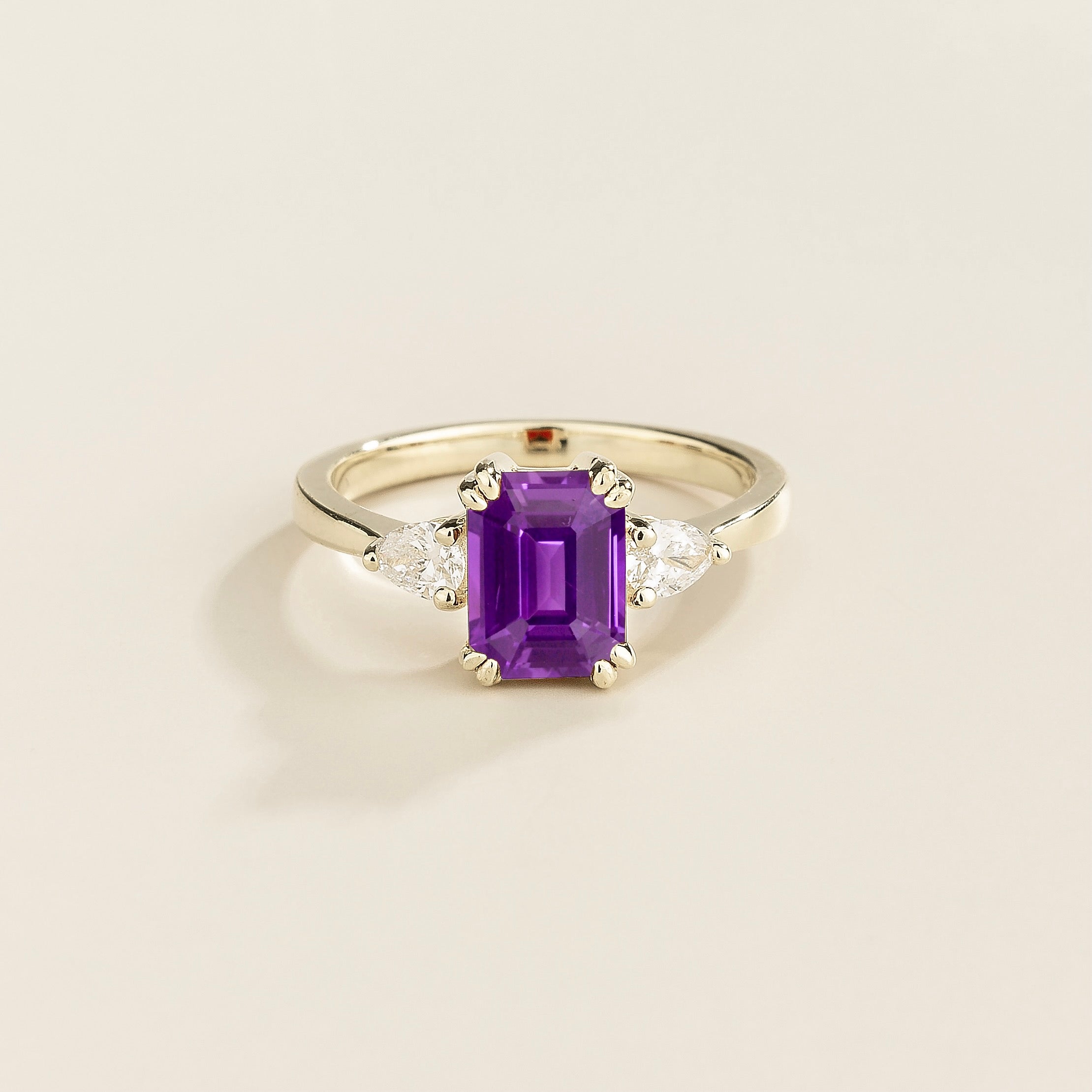A ring with a purple sapphire center stone and pear shape diamonds set in white gold, emerald/octagon cut for the sapphire.
