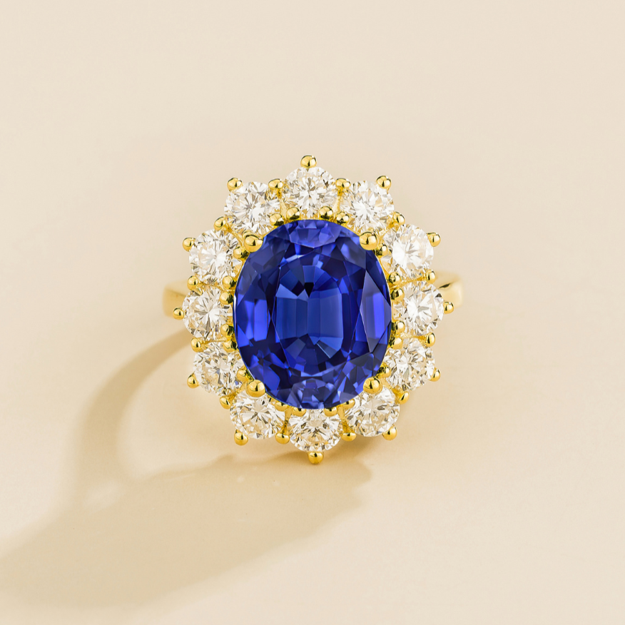 Juvetti yellow gold halo ring featuring an oval lab-grown royal blue sapphire surrounded by round lab-grown diamonds.