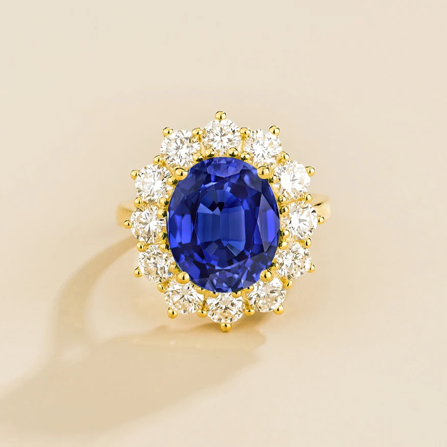 Juvetti yellow gold halo ring featuring an oval lab-grown royal blue sapphire surrounded by round lab-grown diamonds.