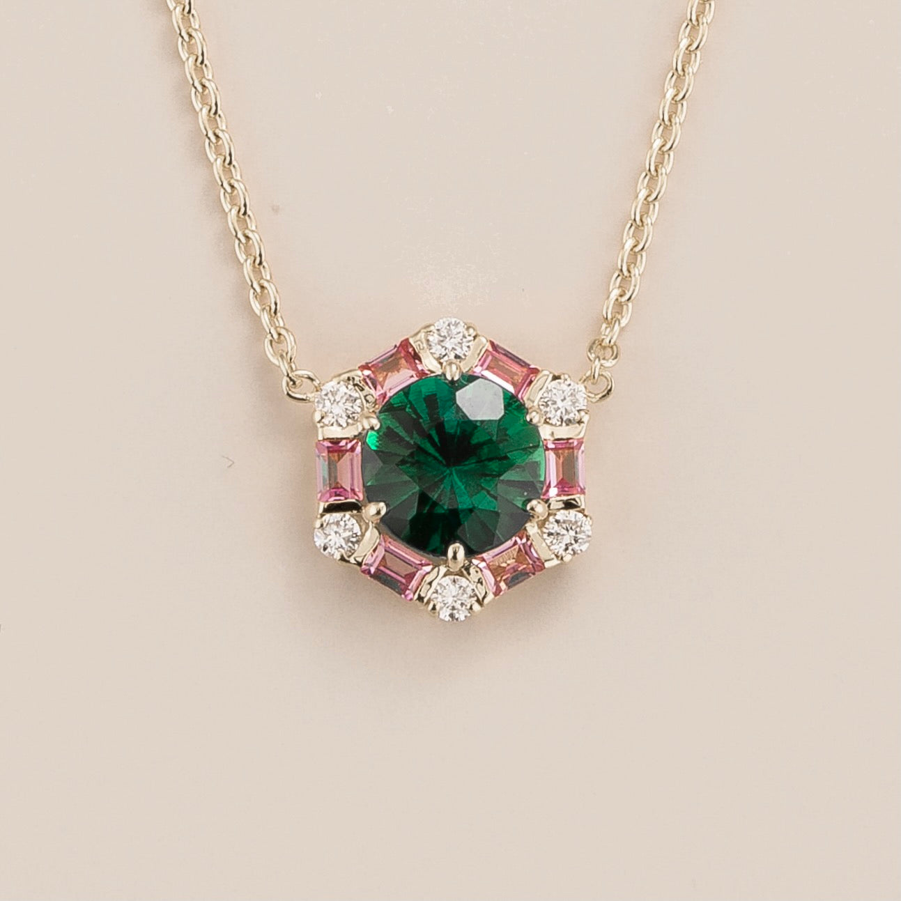 A white gold necklace set with a central emerald pendant, flanked by pink sapphire stones, and adorned with small diamonds, on a plain background.