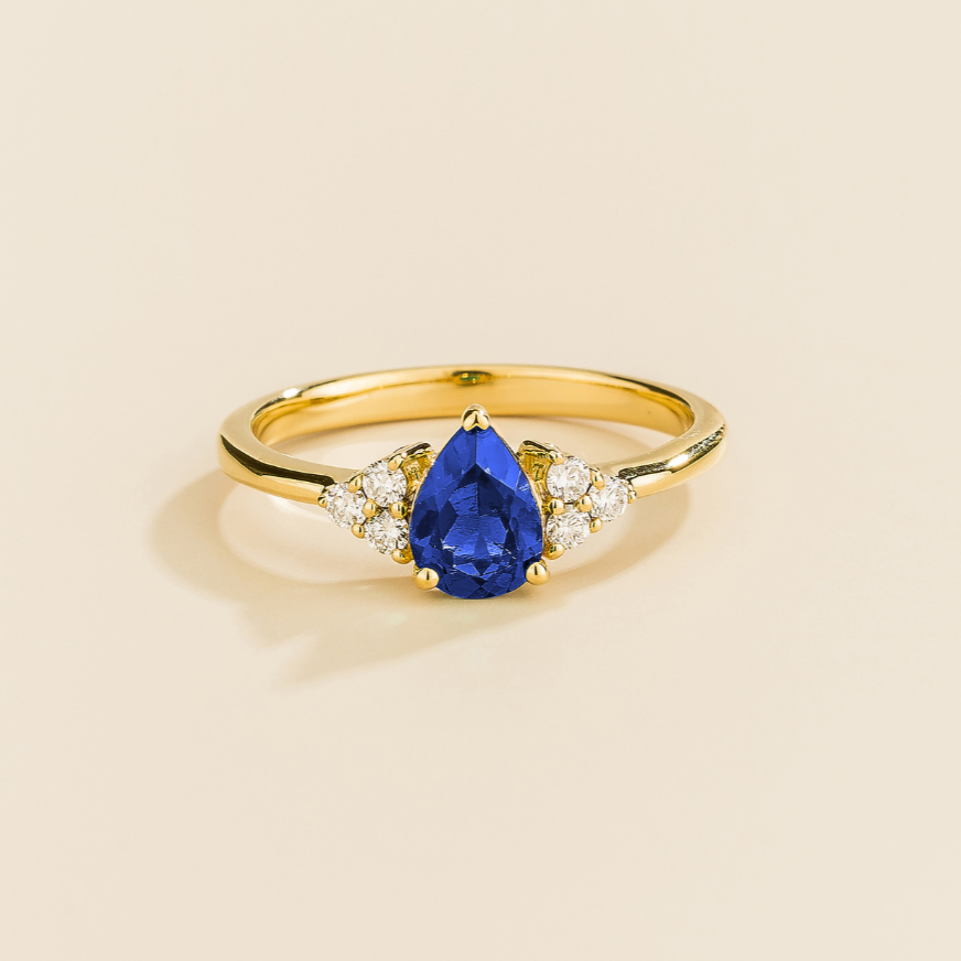 Juvetti yellow gold ring featuring a pear-cut lab-grown royal blue sapphire with lab-grown diamond side stones.