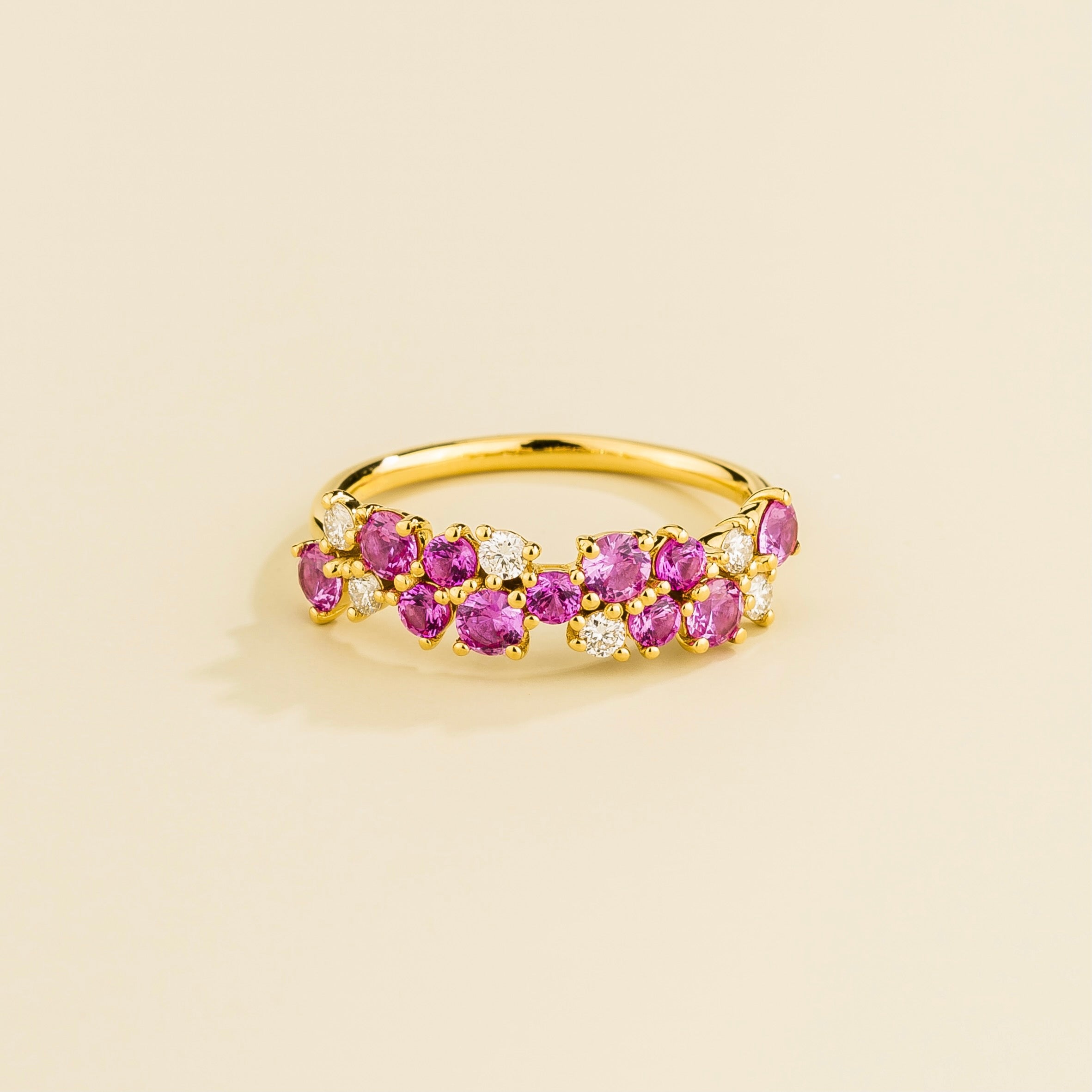 A gold ring with a band of cluster round pink sapphires and round diamonds set in yellow gold.