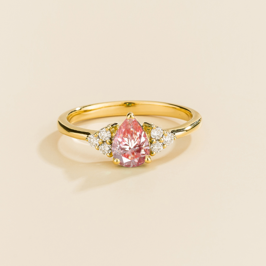 Juvetti yellow gold ring featuring a pear-cut lab-grown padparadscha sapphire with lab-grown diamond side stones.