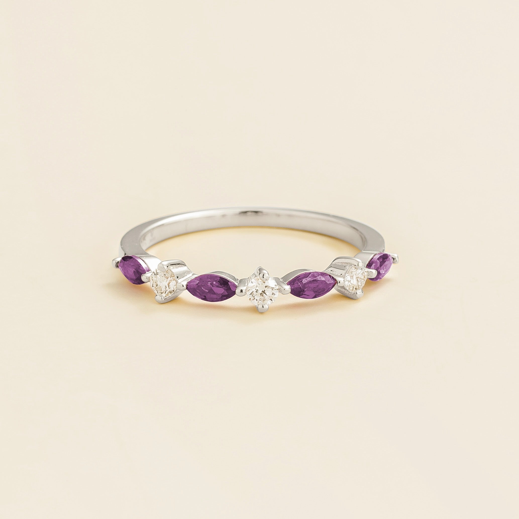 A white gold band ring with marquise cut purple sapphires and round diamonds set on it, displayed against a neutral background.
