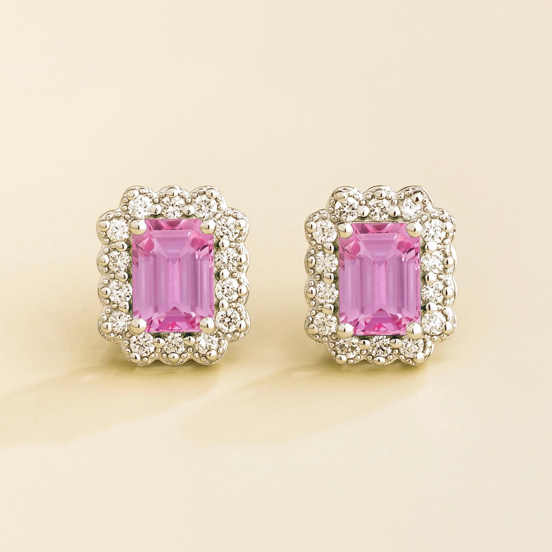 A pair of white gold stud earrings featuring emerald cut pink sapphires surrounded by round diamonds halo.