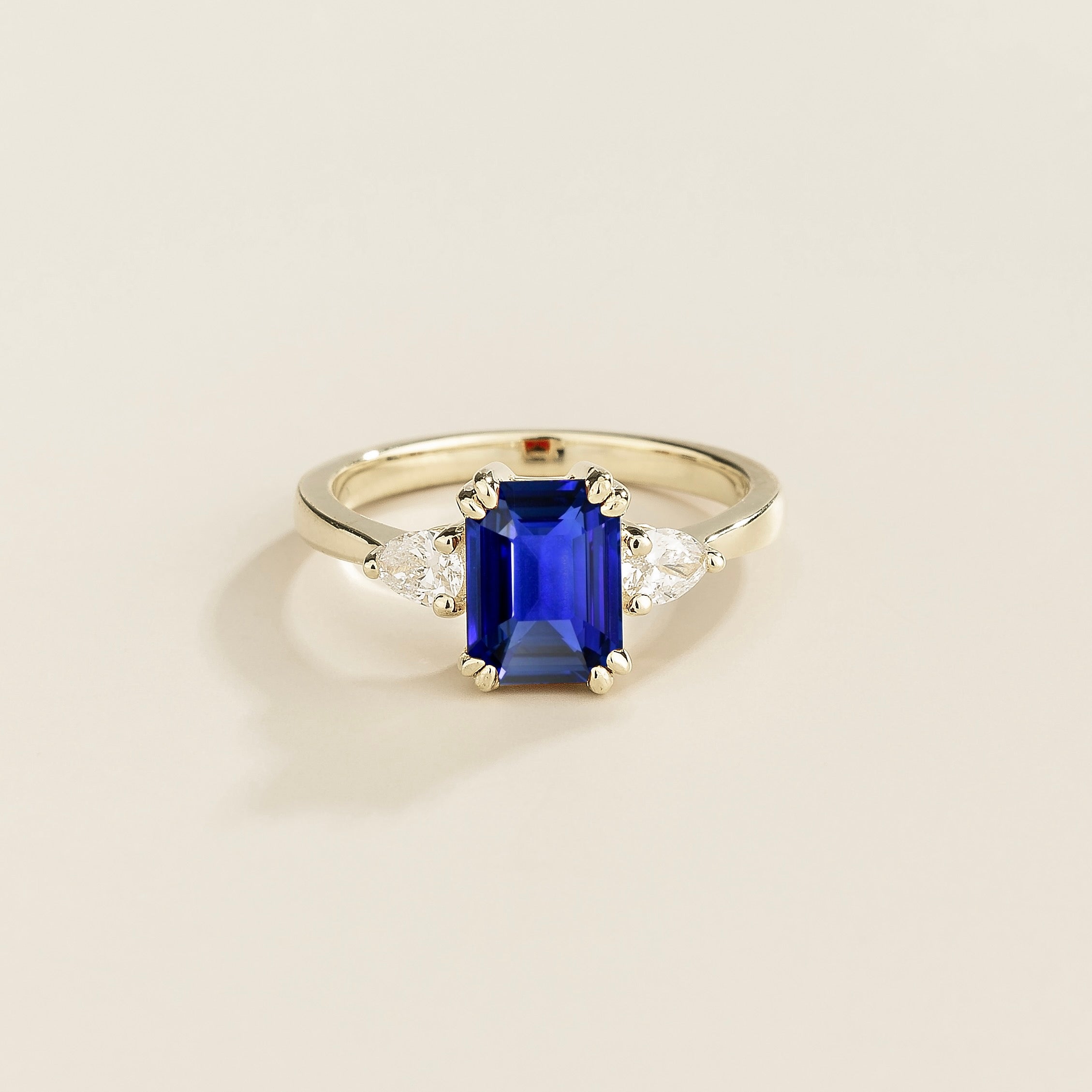 A ring with a blue sapphire center stone and pear shape diamonds set in white gold, emerald/octagon cut for the sapphire.