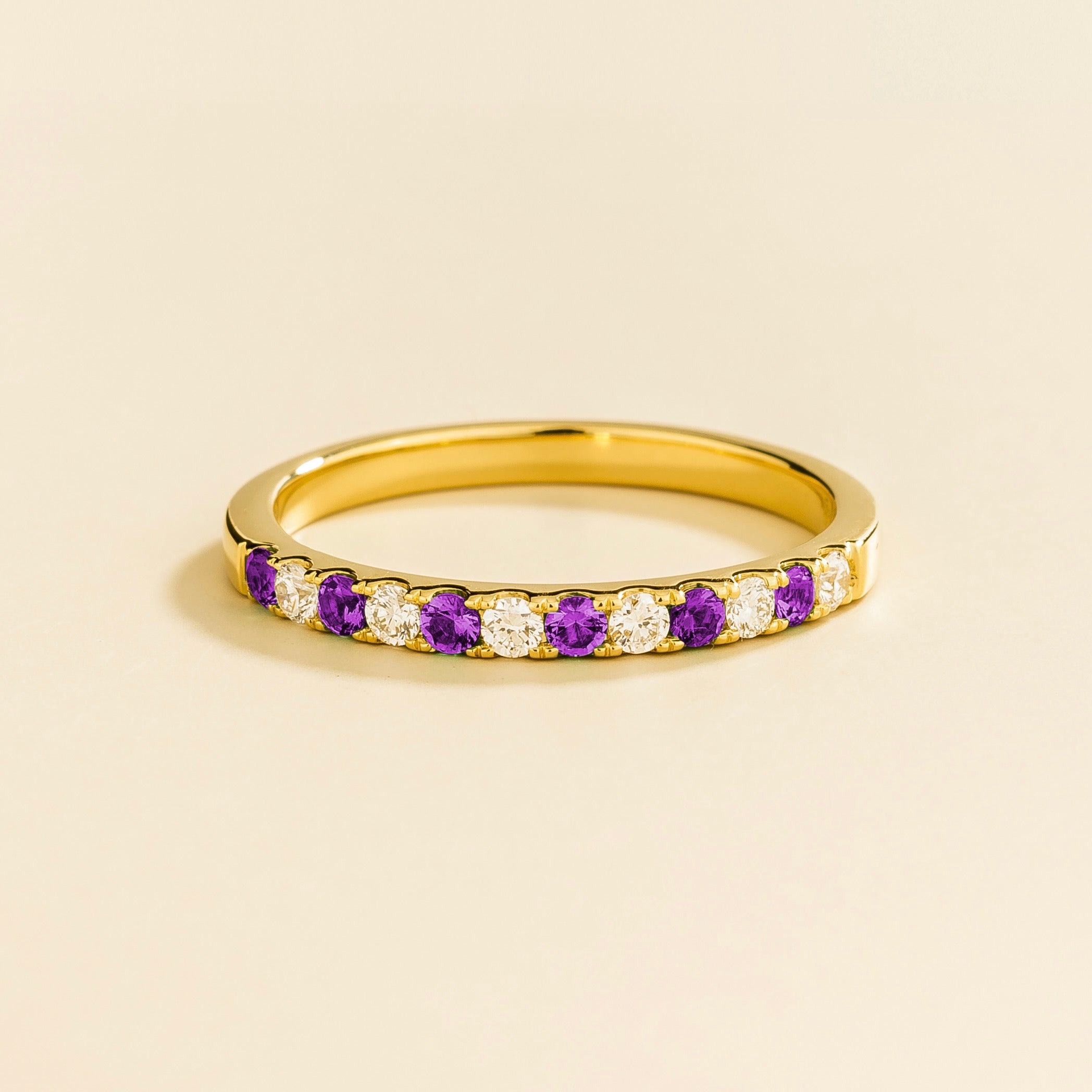 A half eternity gold ring with alternating purple sapphire and diamond elements on a plain background.