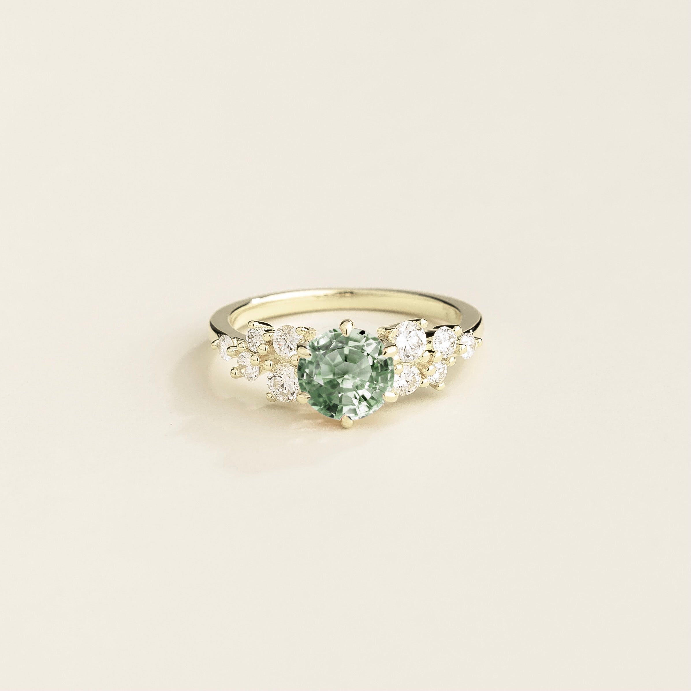 A white gold ring with a green sapphire center stone and smaller diamonds cluster set around it.