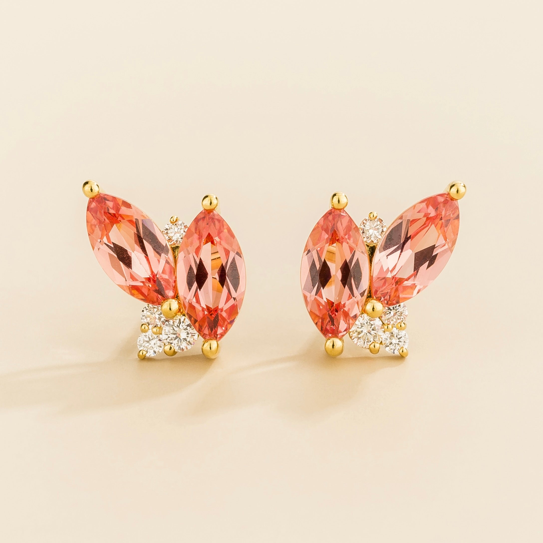 Pair of earrings with marquis padparadscha sapphire gemstones and gold with diamond accents on a light background