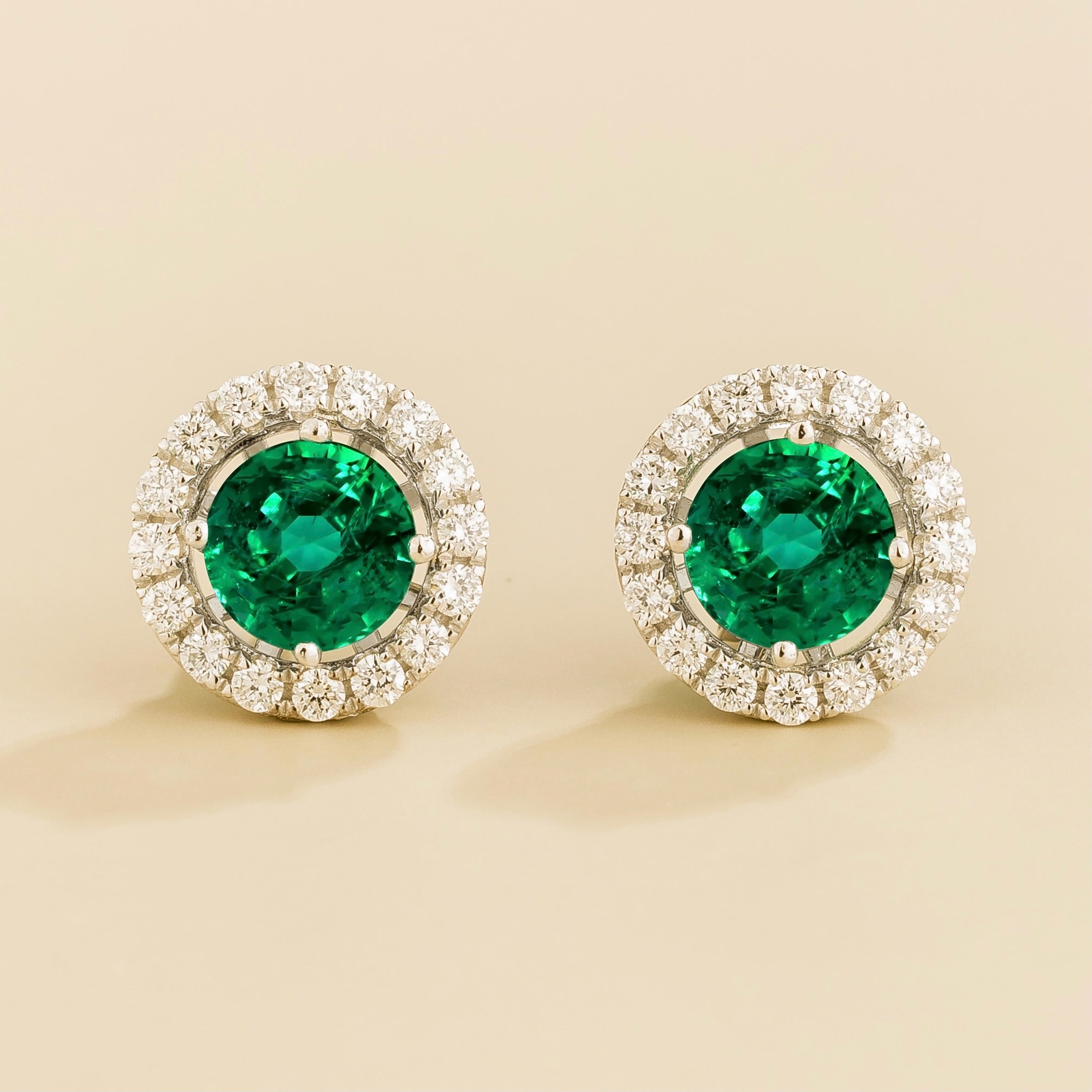 A pair of white gold floret earrings set with emerald centerpiece and surrounding round diamonds halo. Removable halo piece.