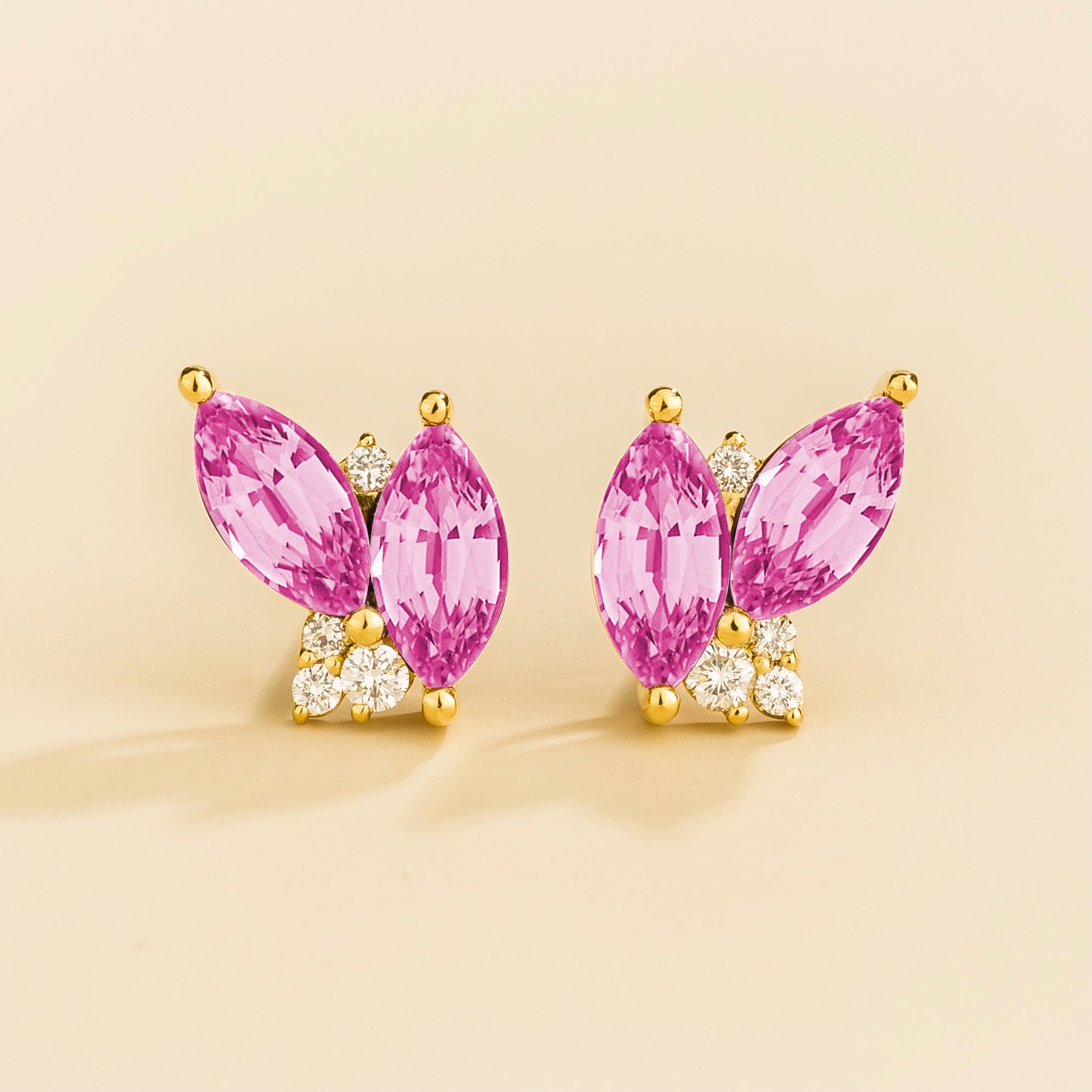 A pair of marquis pink sapphire and round diamond earrings set in gold, with a butterfly-like shape and small round diamonds on the hooks.