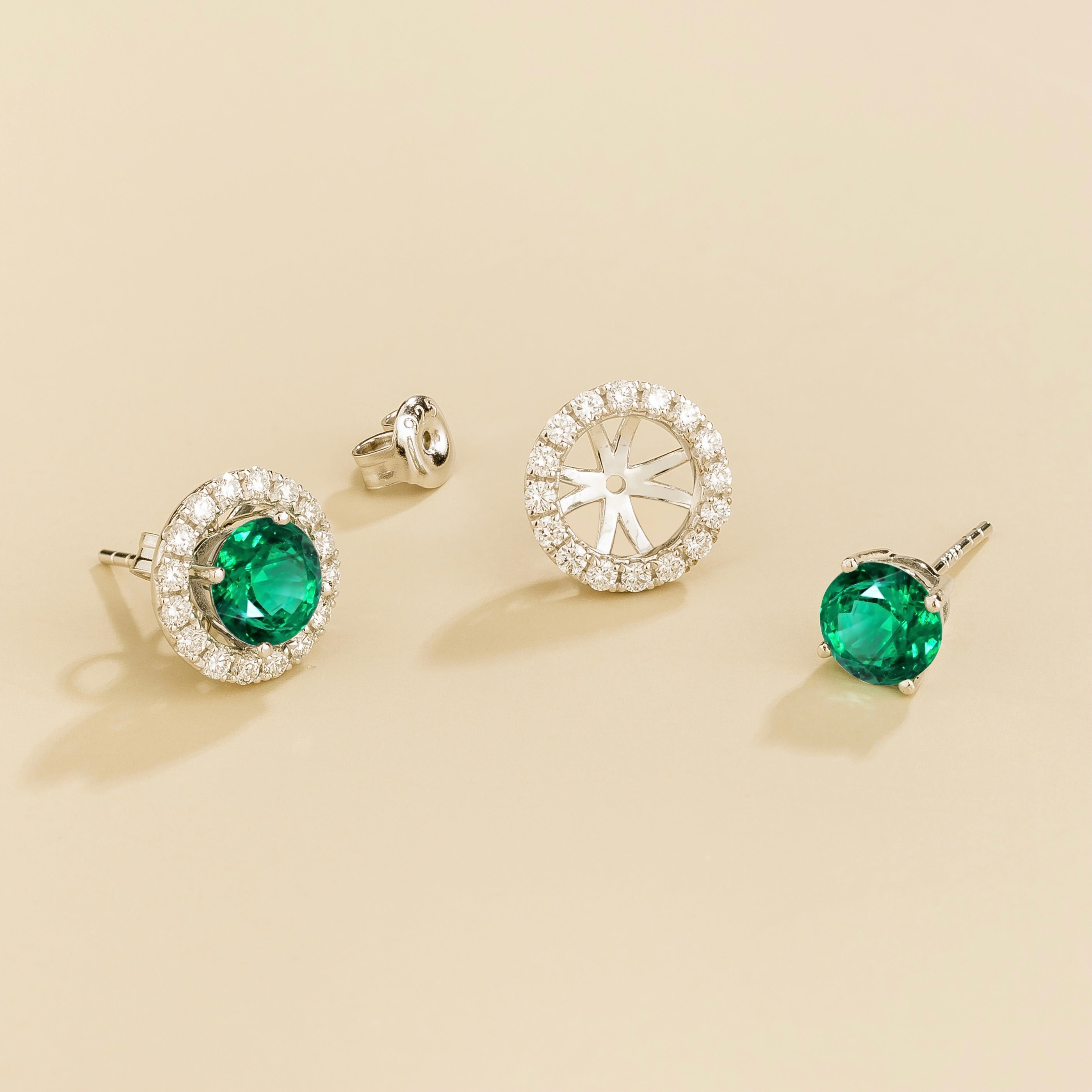 A pair of white gold floret earrings set with emerald centerpiece and surrounding round diamonds halo. Removable halo piece.