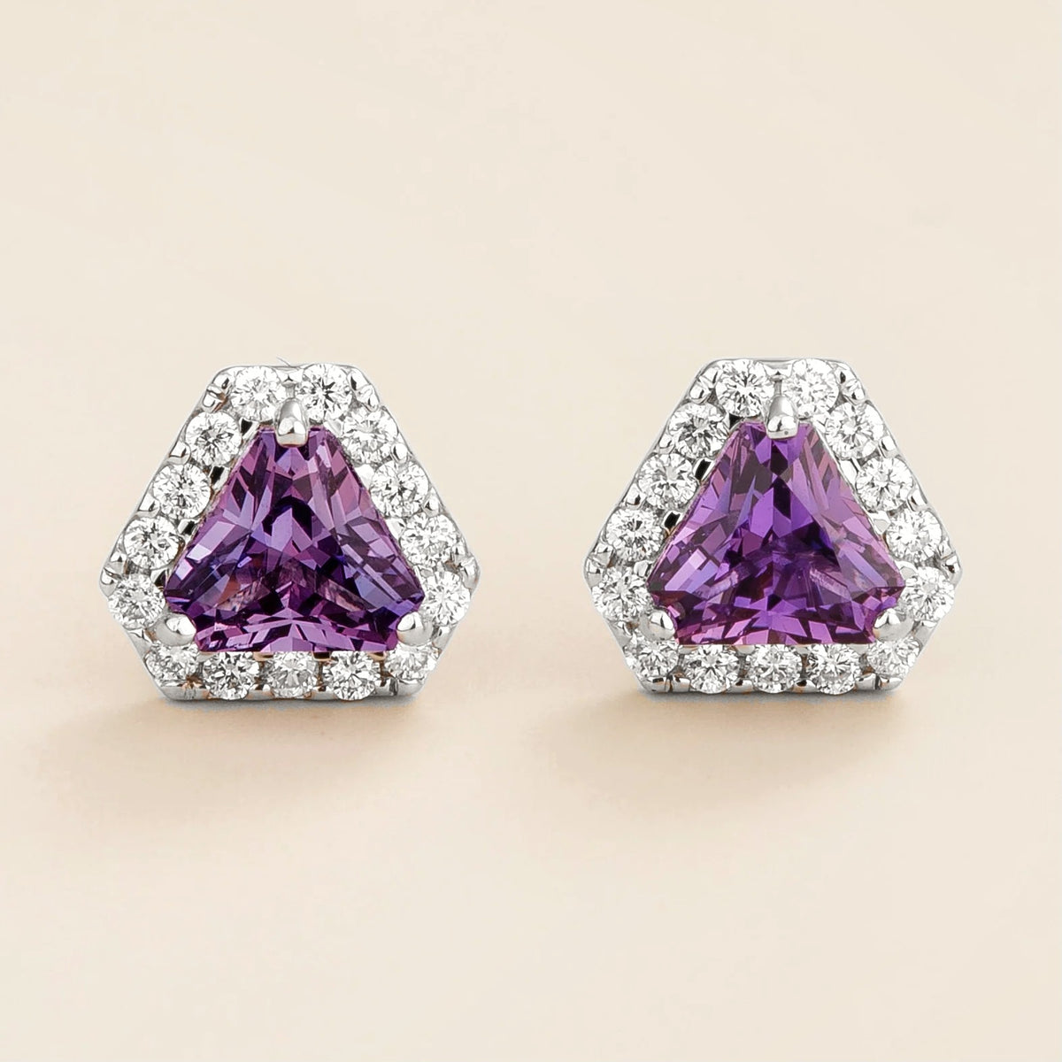 A pair of white gold earrings, with triangle purple sapphire and diamonds halo, both set in a geometric pattern.