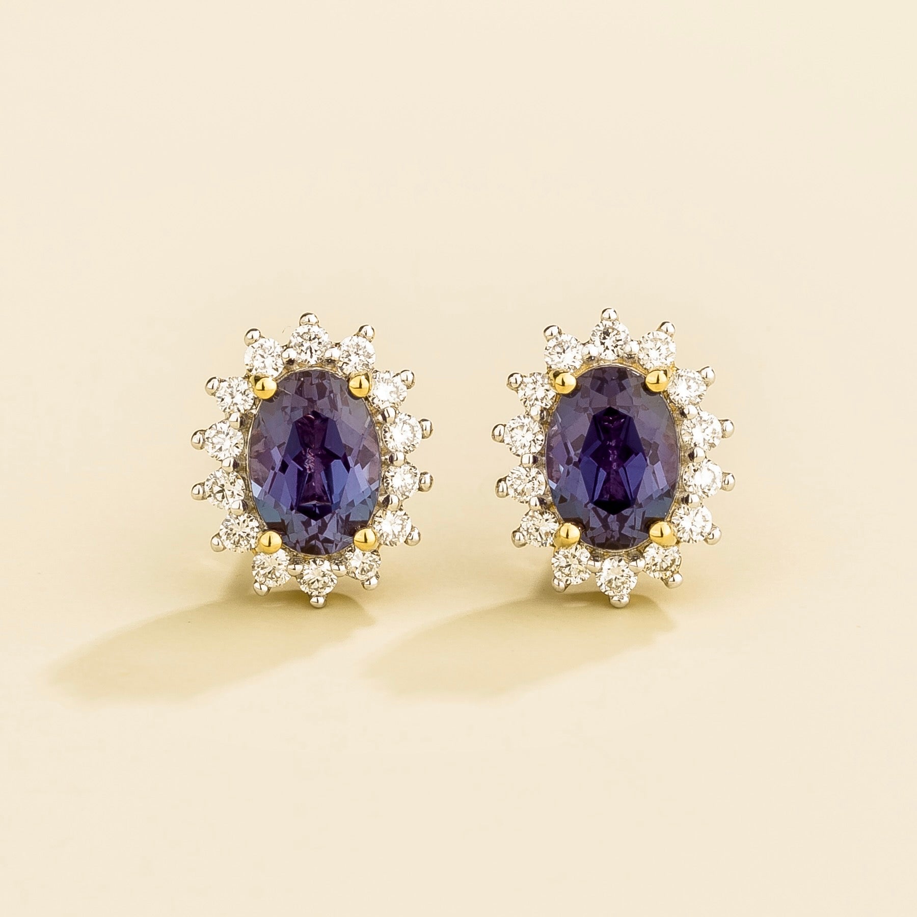 A pair of Divo gold earrings featuring oval-cut Alexandrite gemstones with a halo of smaller round-cut diamonds around each gemstone.