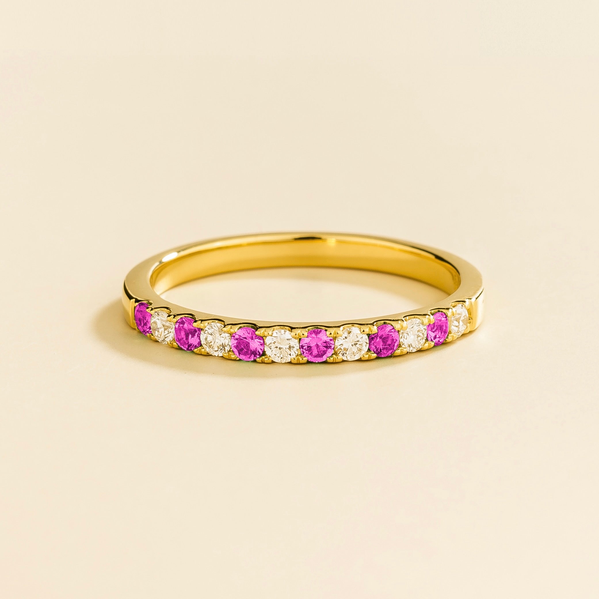 A gold ring with alternating vivid pink sapphire and diamond gemstones, forming a half eternity band design.