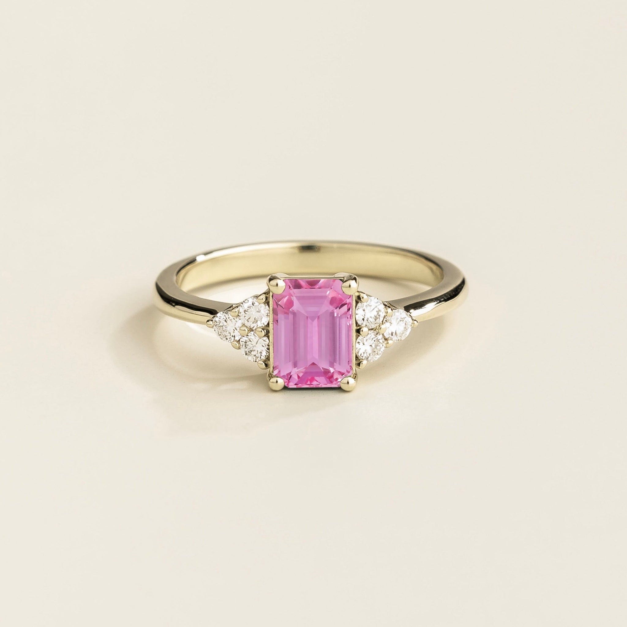 A white gold ring featuring a pink sapphire gemstone and small diamonds, set in a classic six-prong setting on a plain band.