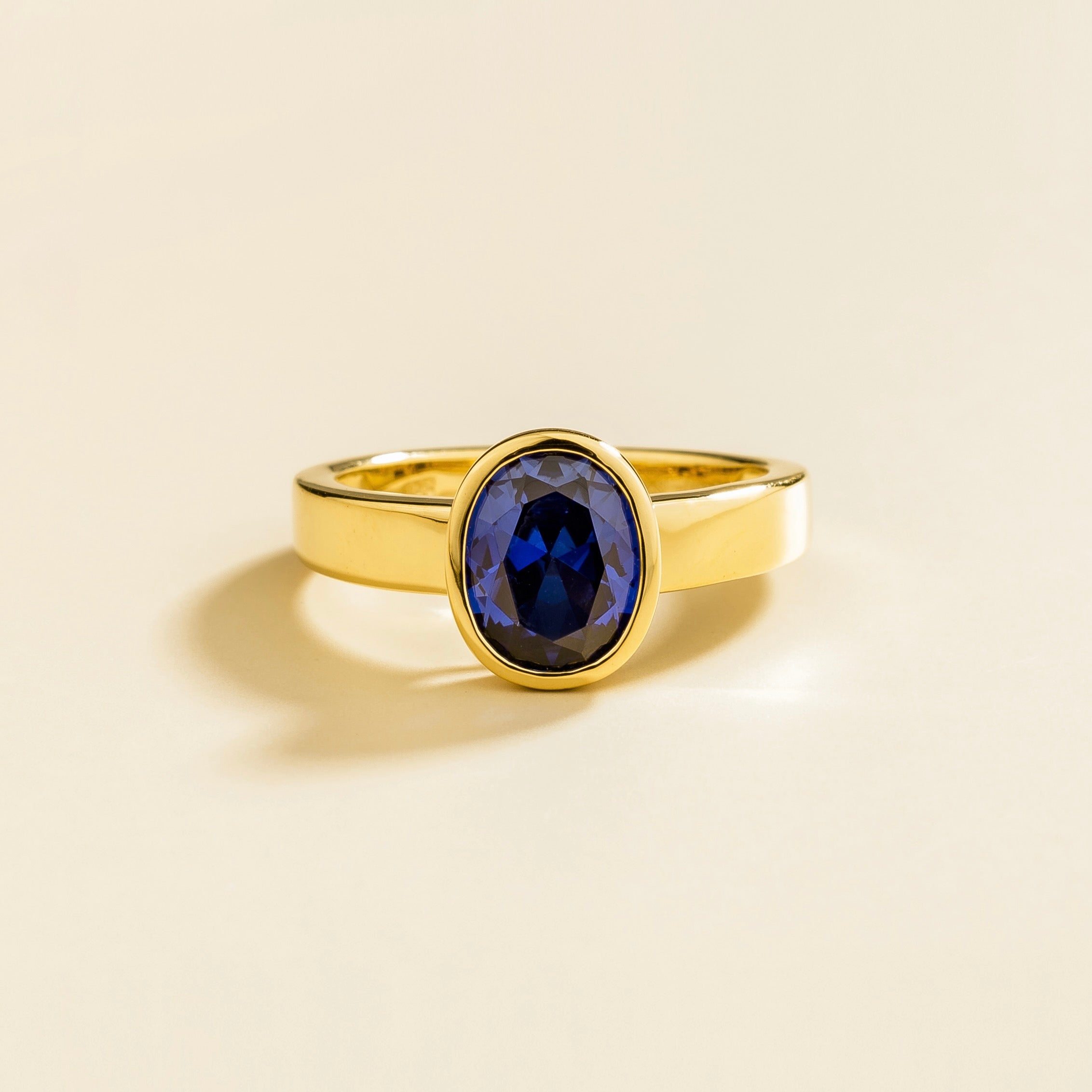 Juvetti yellow gold ring featuring an oval lab-grown blue sapphire in a bezel setting.
