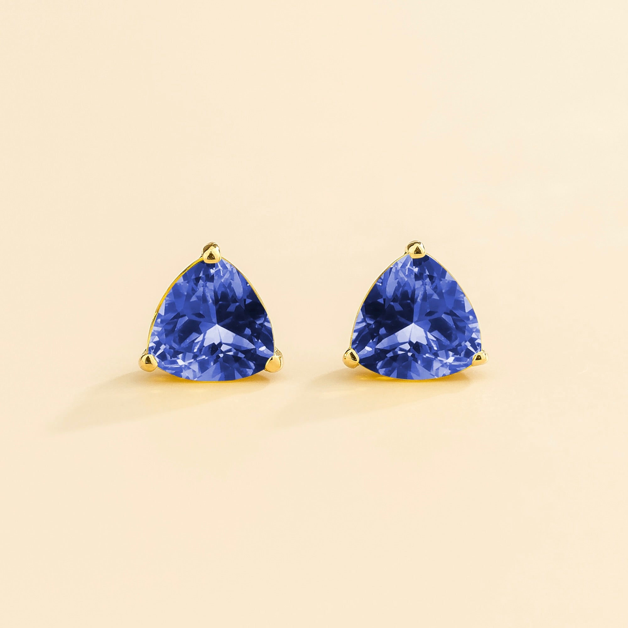 A pair of gold trillion earrings set with blue sapphires, displayed against a neutral background.