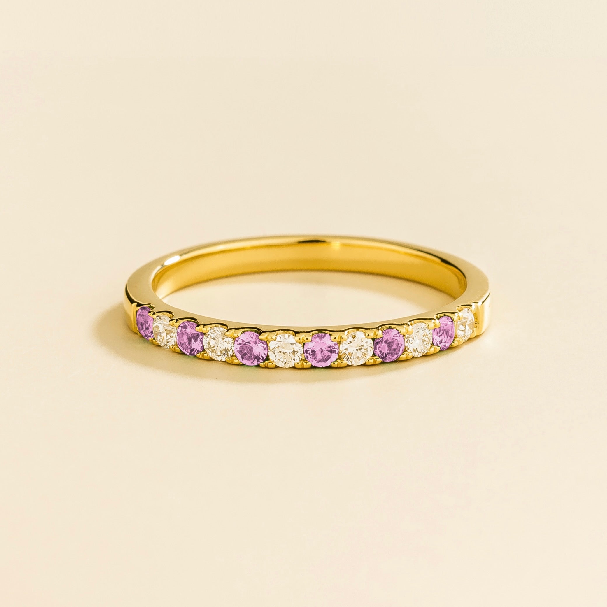 A half eternity gold ring with pastel pink sapphire and diamond accents on a plain background.