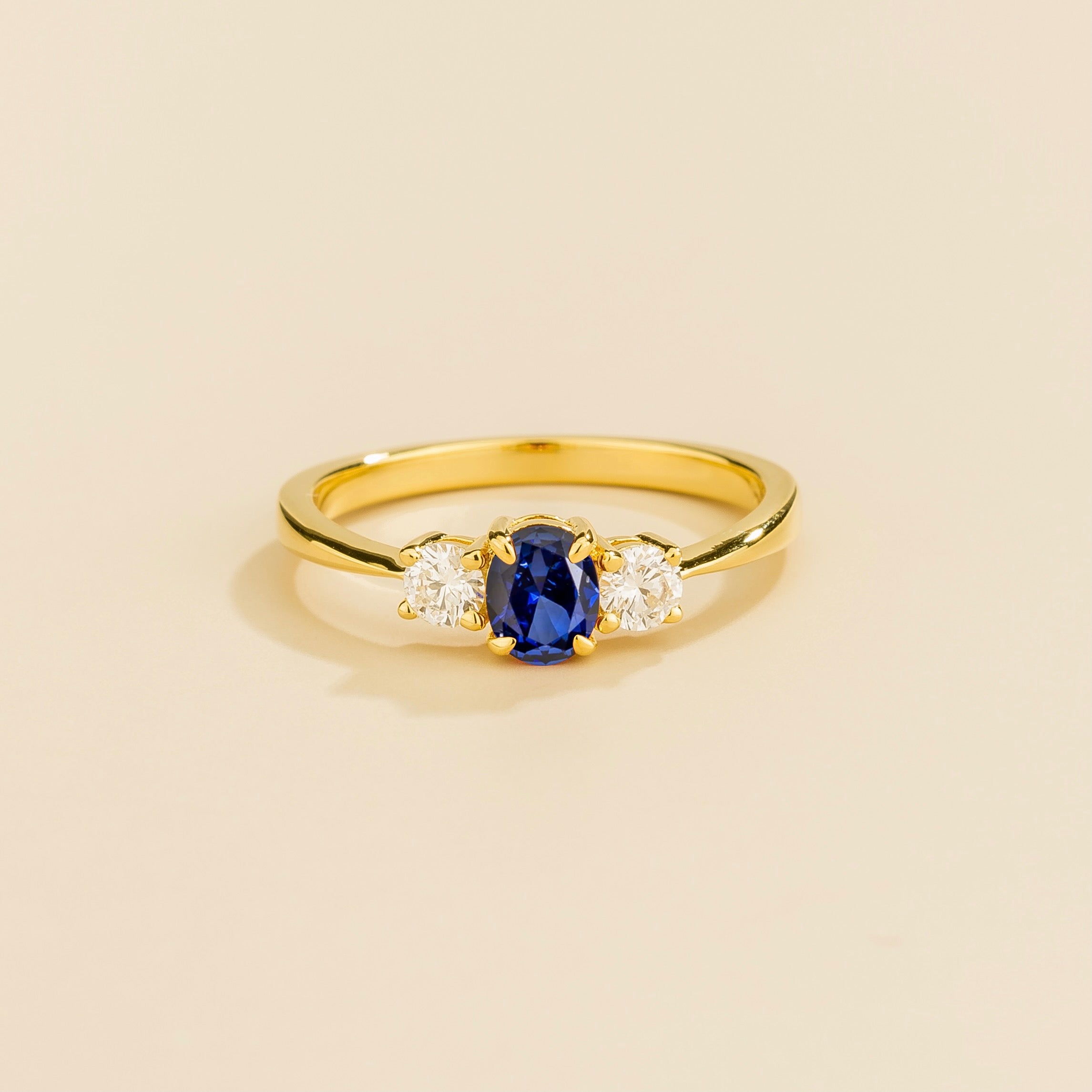 3 gemstones gold ring featuring a central blue sapphire gemstone flanked by two white diamonds on a yellow gold band.