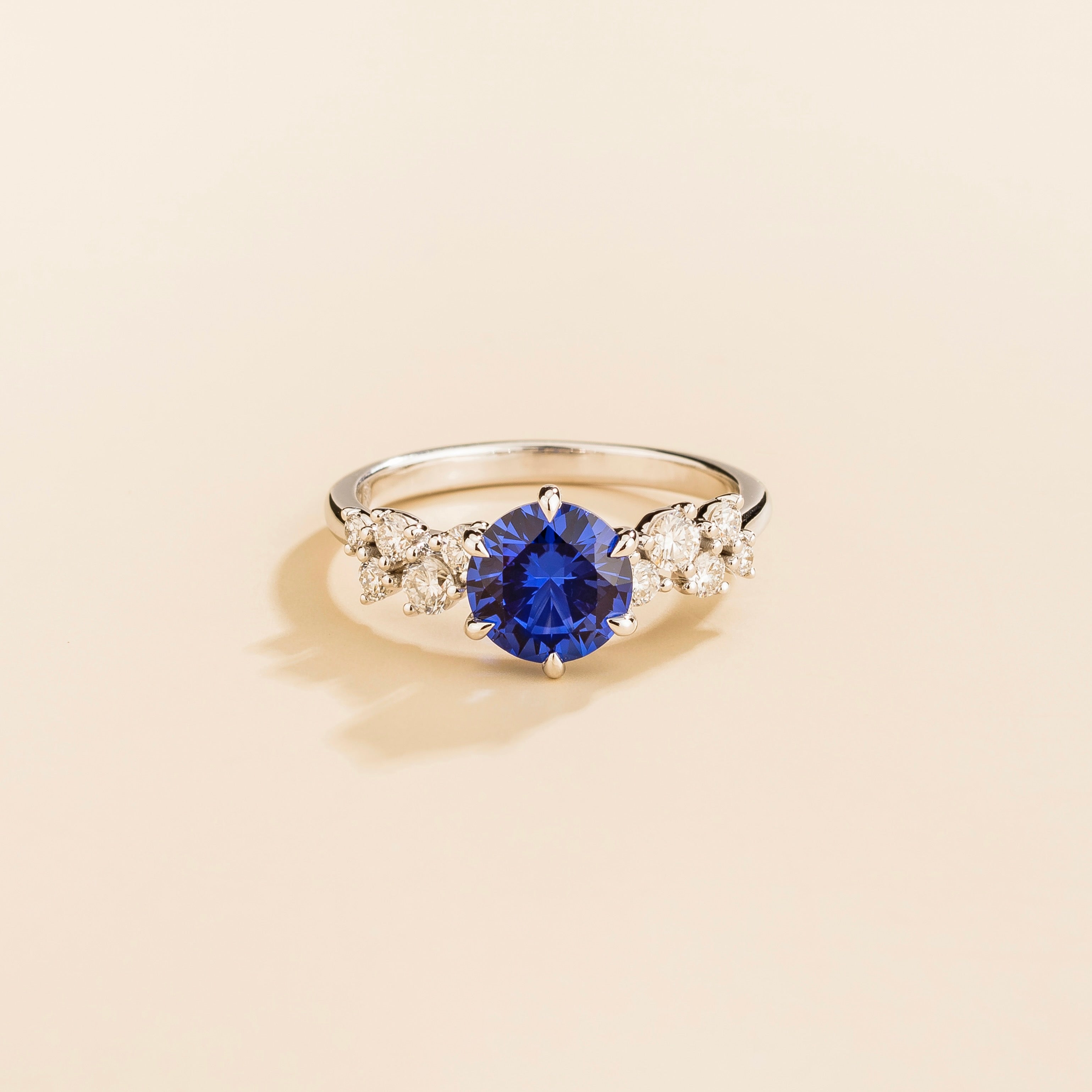 A white gold ring with a blue sapphire center stone and smaller diamonds cluster set in gold, displayed against a neutral background.