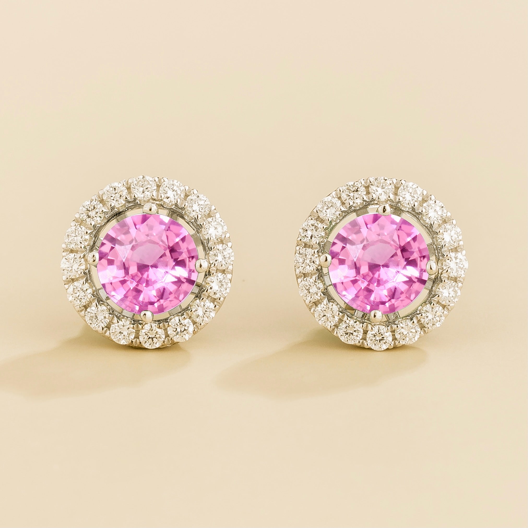 A pair of white gold floret earrings set with a round pink sapphire centerpiece and surrounding round diamonds halo. Removable halo piece.