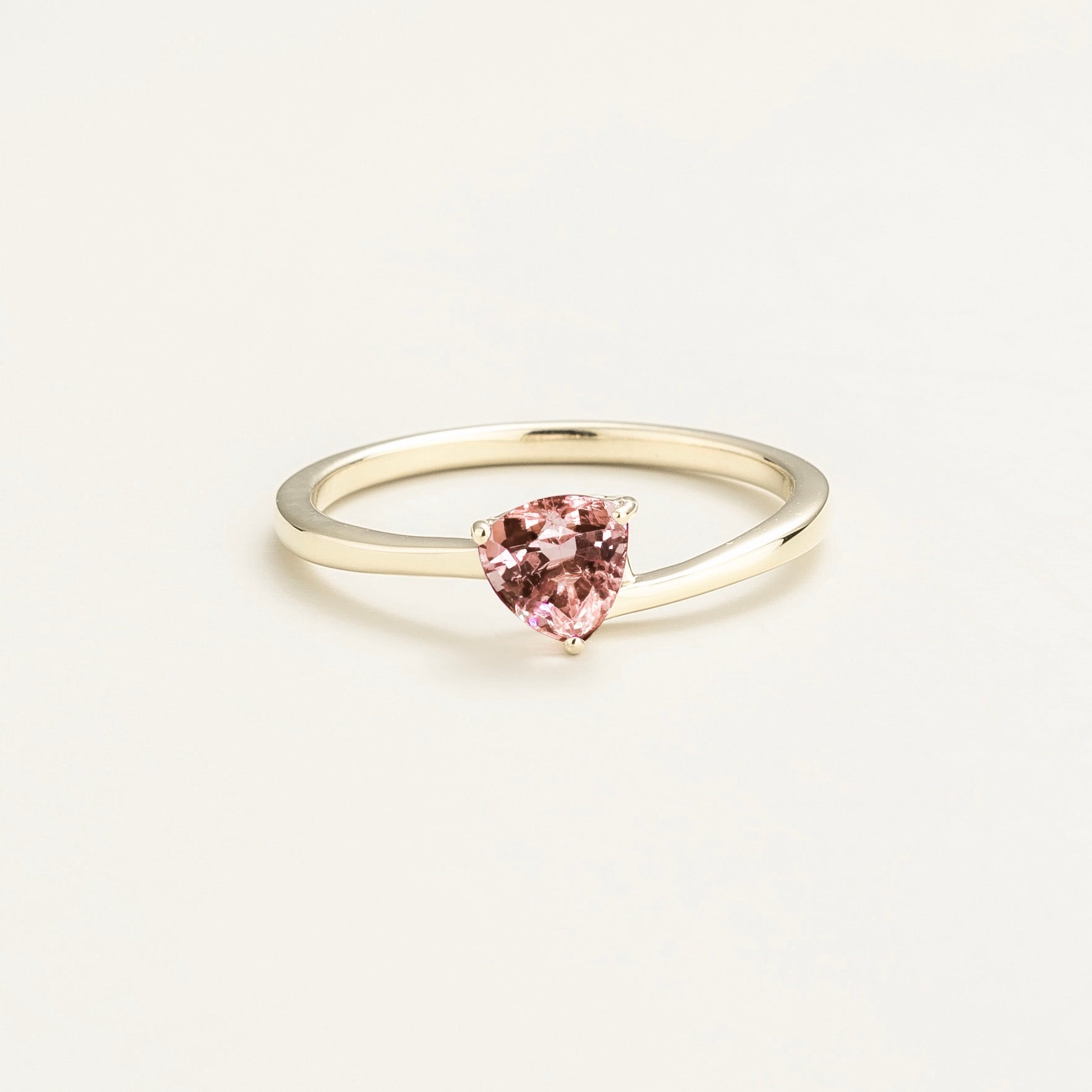 A white gold ring with a trillion-cut morganite centerpiece, set in a modern curved setting on a plain background.