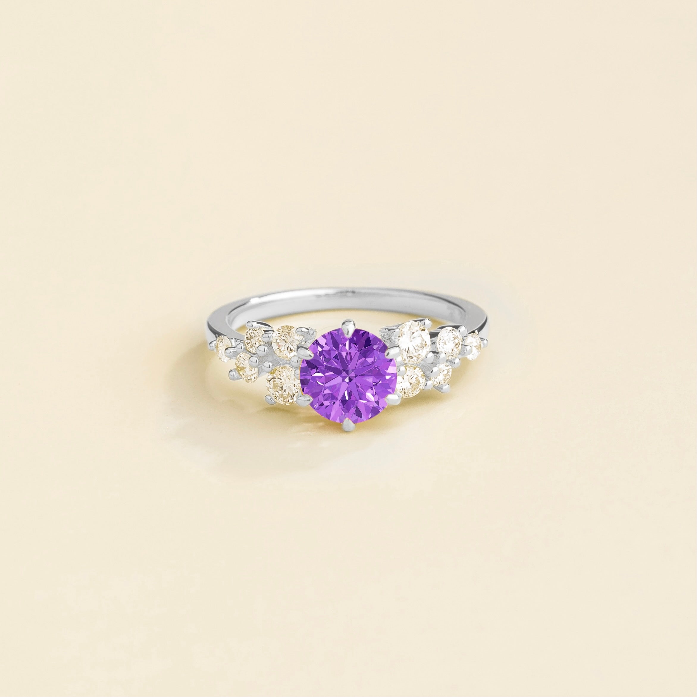 A white gold ring with a purple sapphire center stone and smaller diamonds cluster set in gold, displayed against a neutral background.