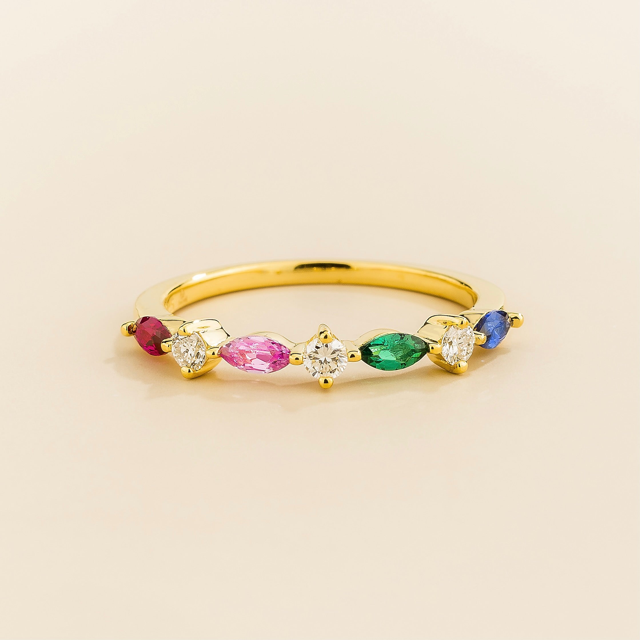 A gold band ring with marquise cut ruby, pink sapphire, emerald, blue sapphire and round cut diamonds set in an alternating pattern on a plain