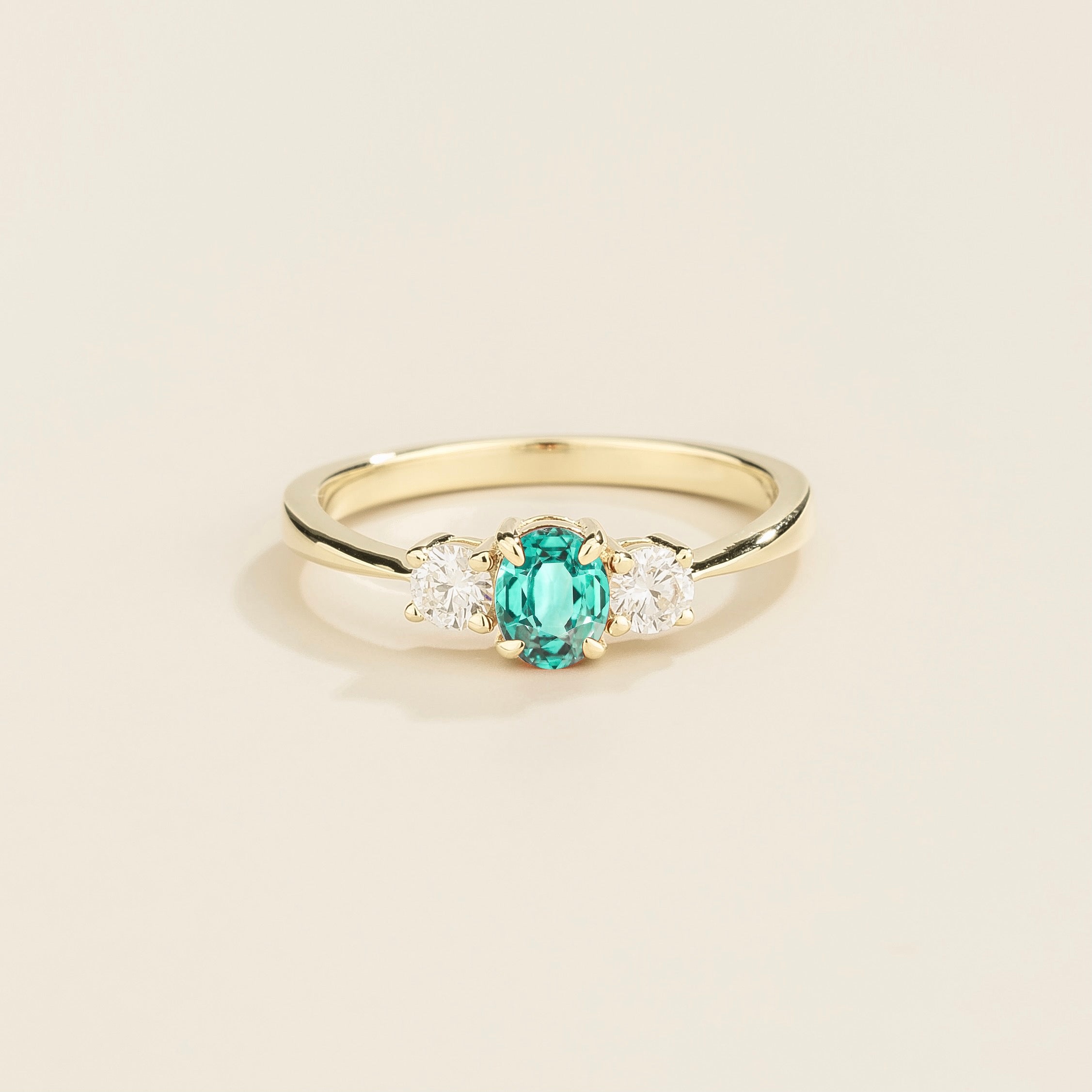 A white gold 3 gemstone ring featuring a central Paraiba sapphire with flanking diamonds, viewed from the front against a plain background.
