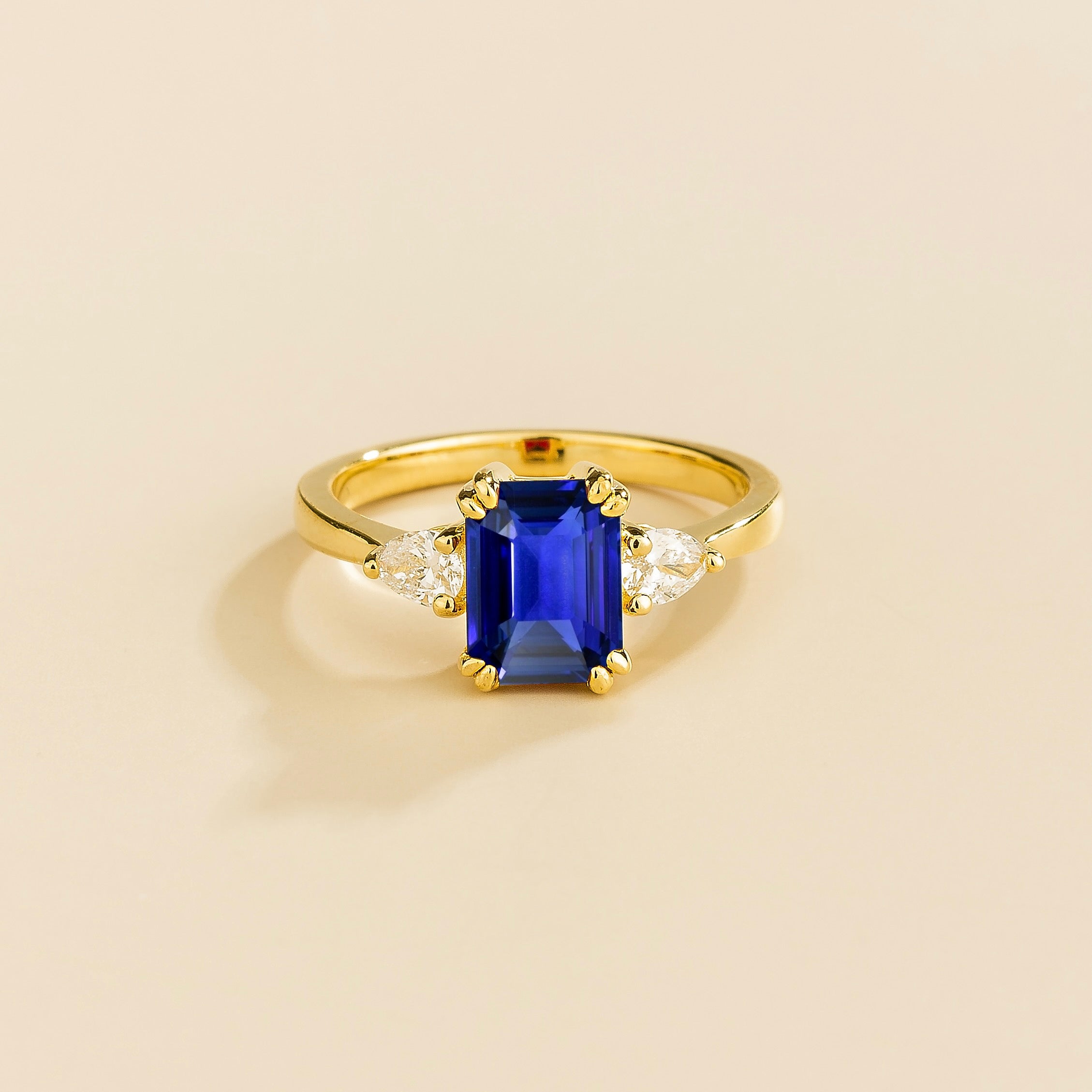 A gold ring with a blue sapphire center stone and pear shape diamonds set in yellow gold, emerald cut for the sapphire.