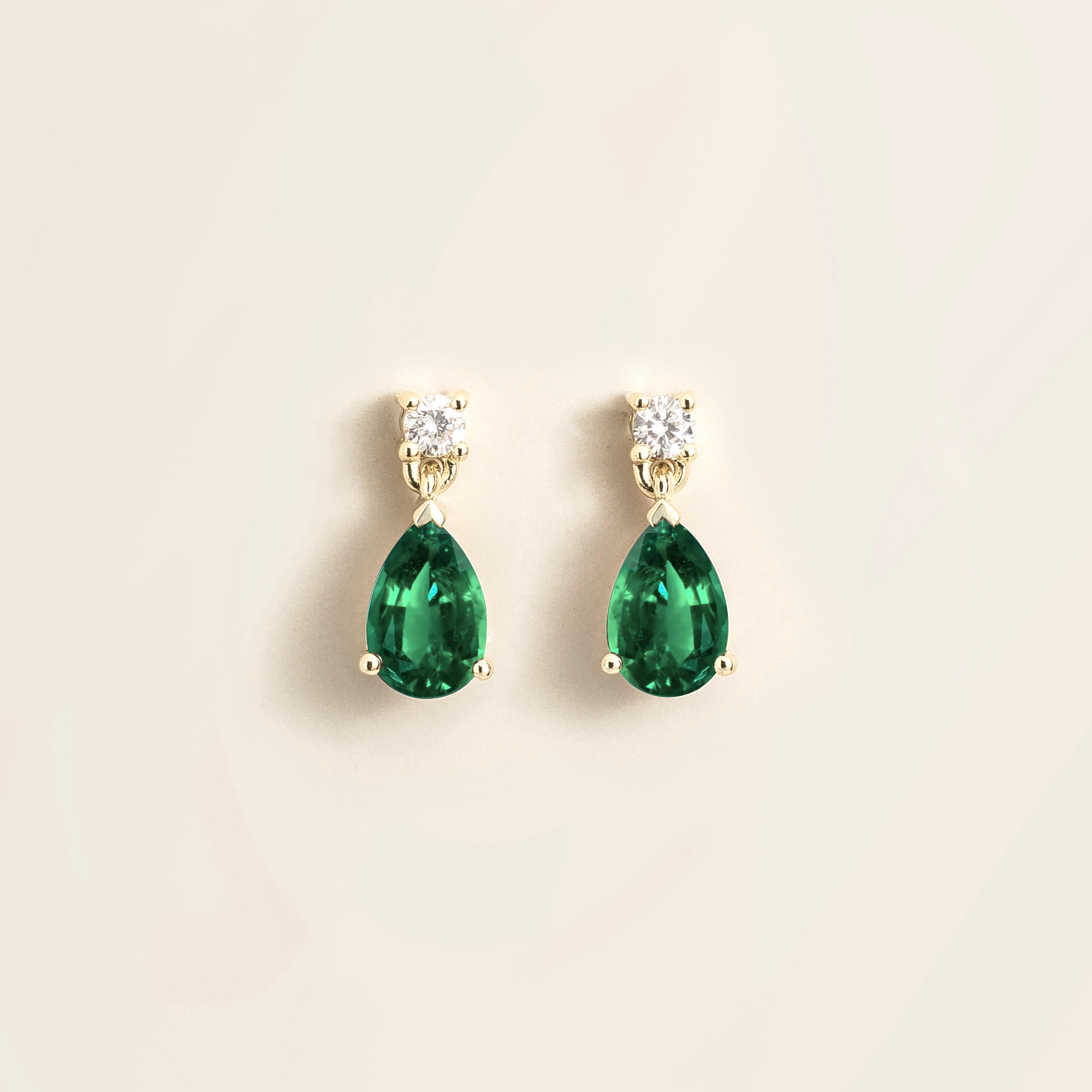 A pair of white gold drop earrings set with pear shape emerald and round diamond gemstones.