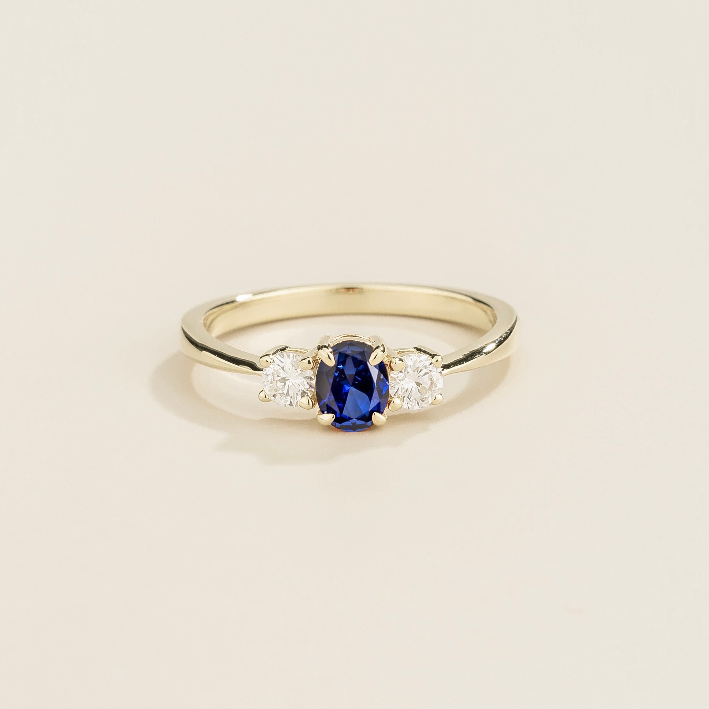 3 gemstones white gold ring with a central blue sapphire gemstone flanked by two smaller diamond gemstones on each side.