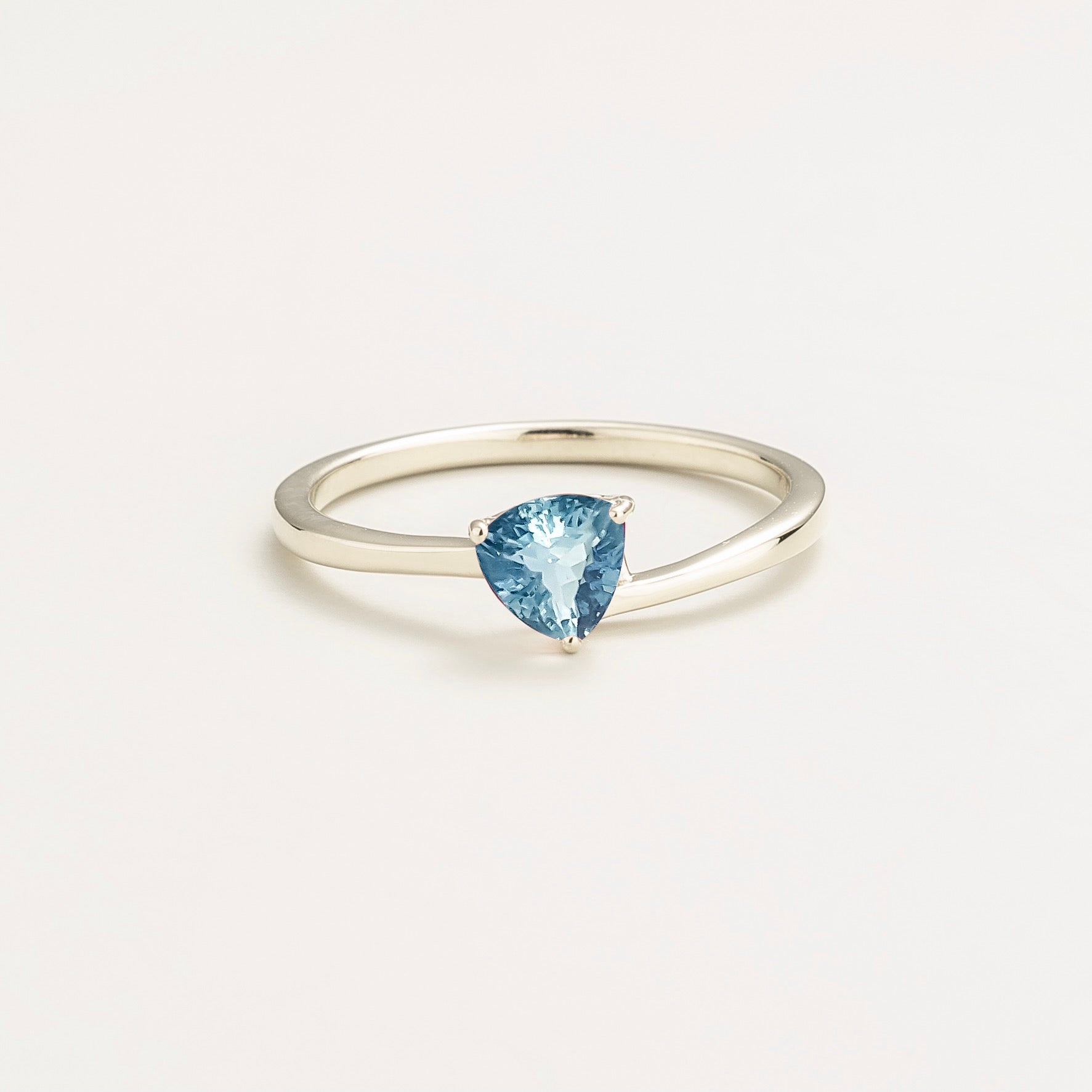 A solitaire white gold ring featuring a trillion-cut aquamarine in a unique modern curved setting.