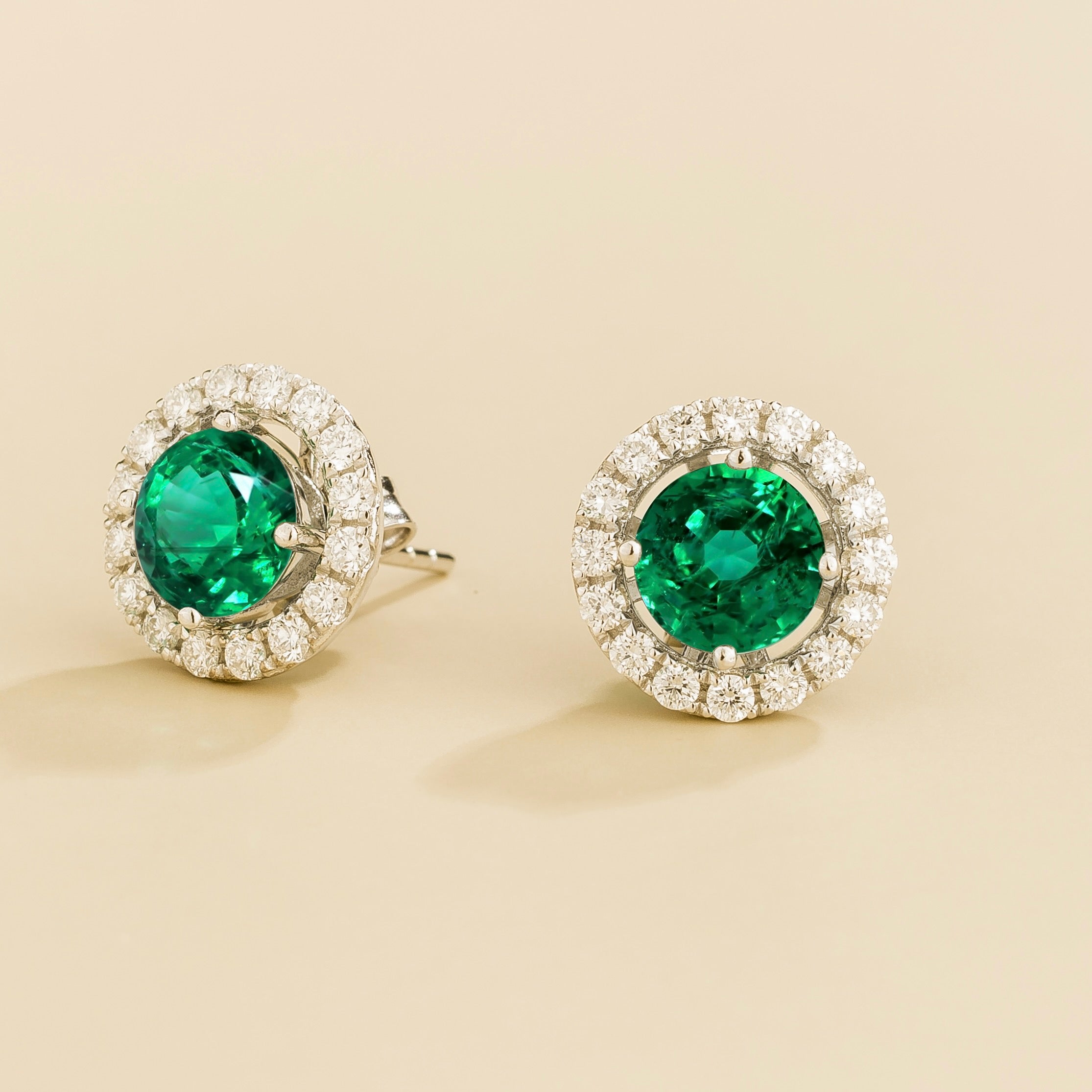 A pair of white gold floret earrings set with emerald centerpiece and surrounding round diamonds halo. Removable halo piece.