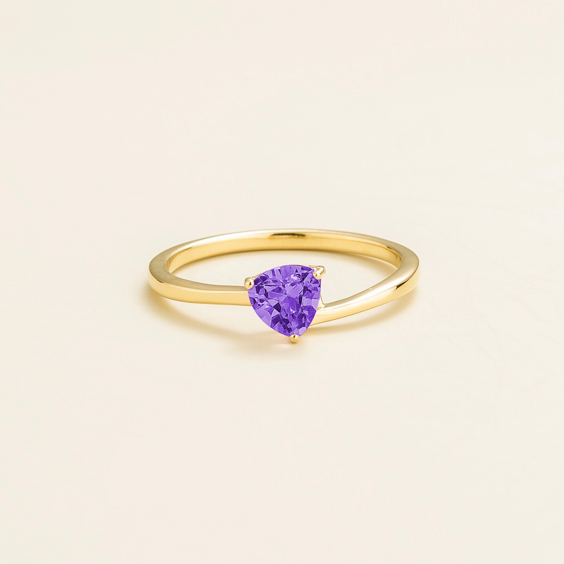 A solitaire gold ring with a trillion-cut purple sapphire centerpiece set in a modern curved band.