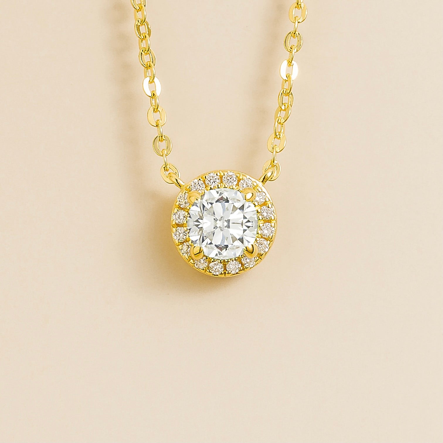 Gold necklace with a round diamond pendant and diamond halo on a beige background