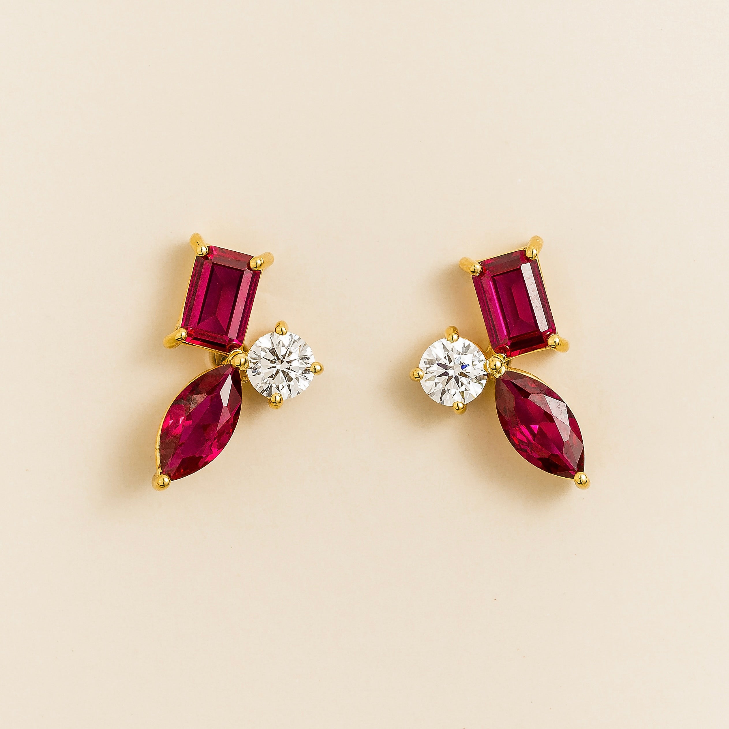 Pair of yellow gold stud earrings with emerald-cut and marquise rubies accented by round diamonds in a geometric three-stone design.