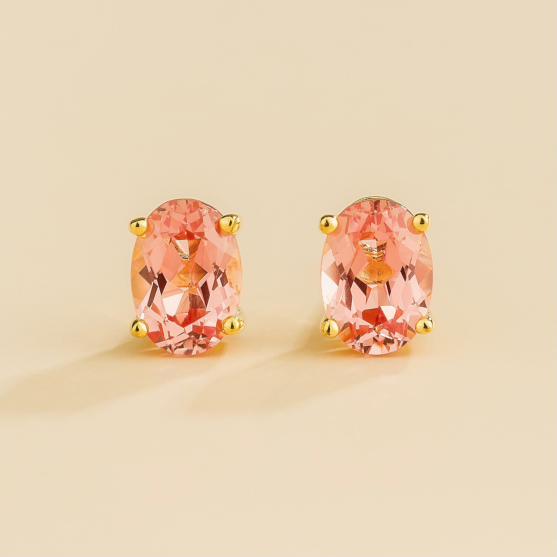 A pair of stud gold earrings set with oval Padparadscha sapphires.