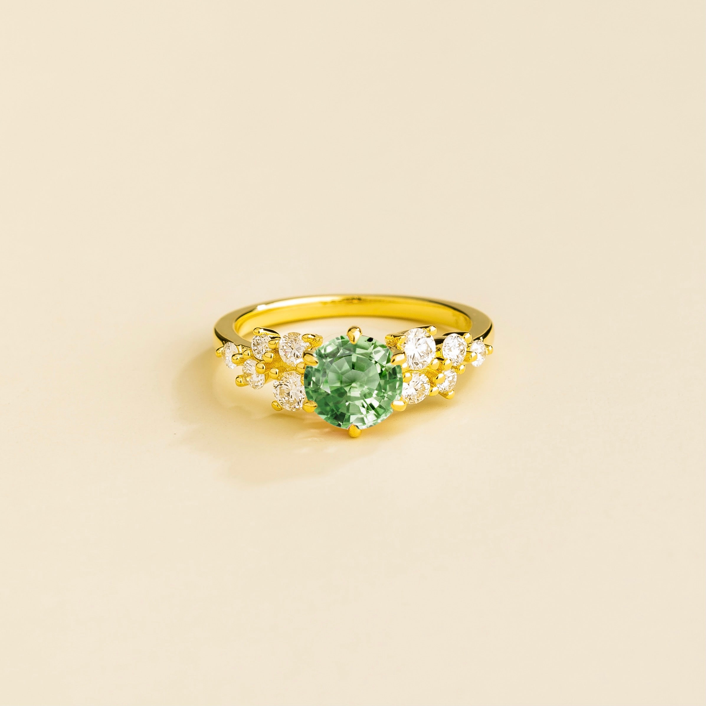 A gold ring with a green sapphire center stone and smaller diamonds cluster set in gold, displayed against a neutral background.