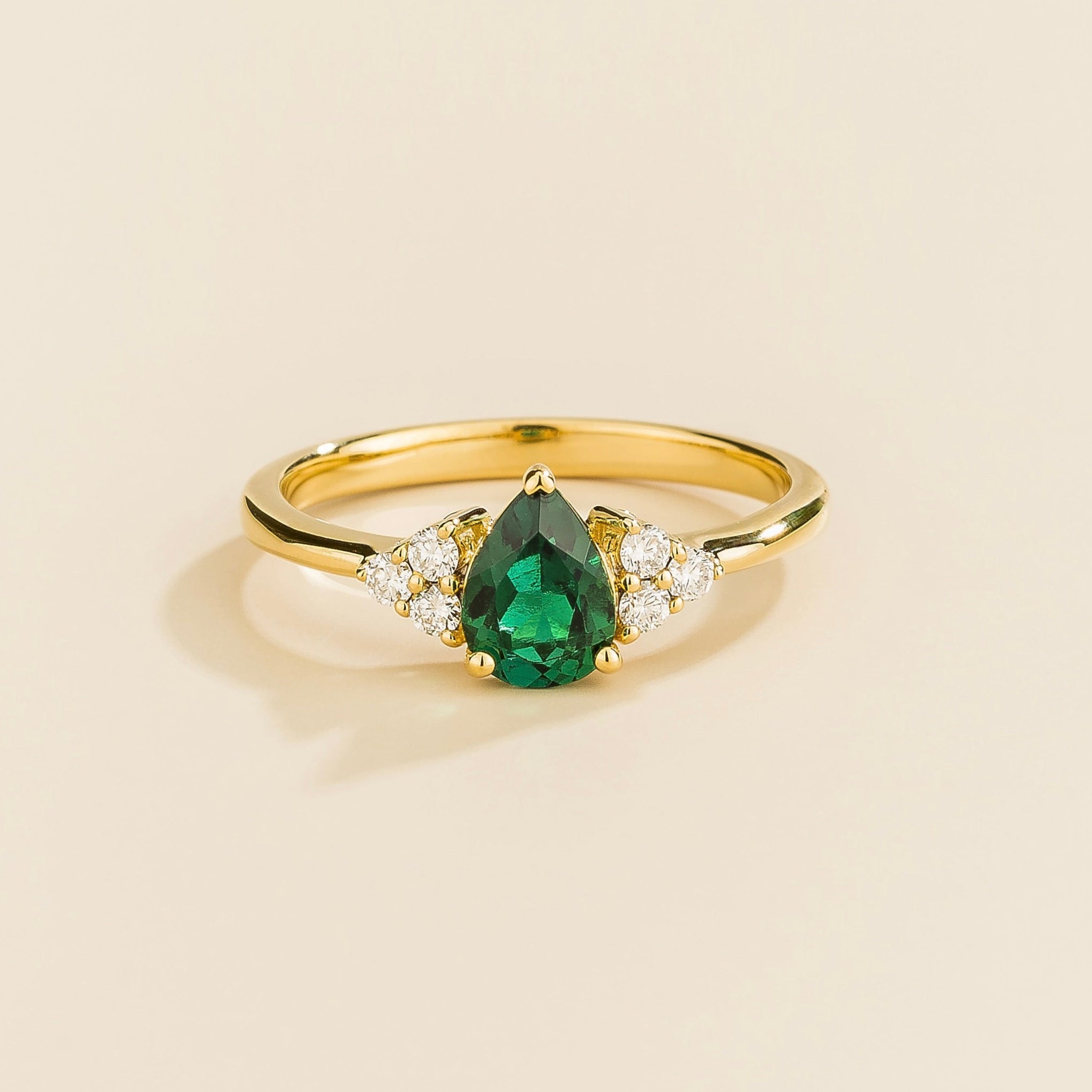 Juvetti yellow gold ring featuring a pear-cut lab-grown emerald with lab-grown diamond side stones.