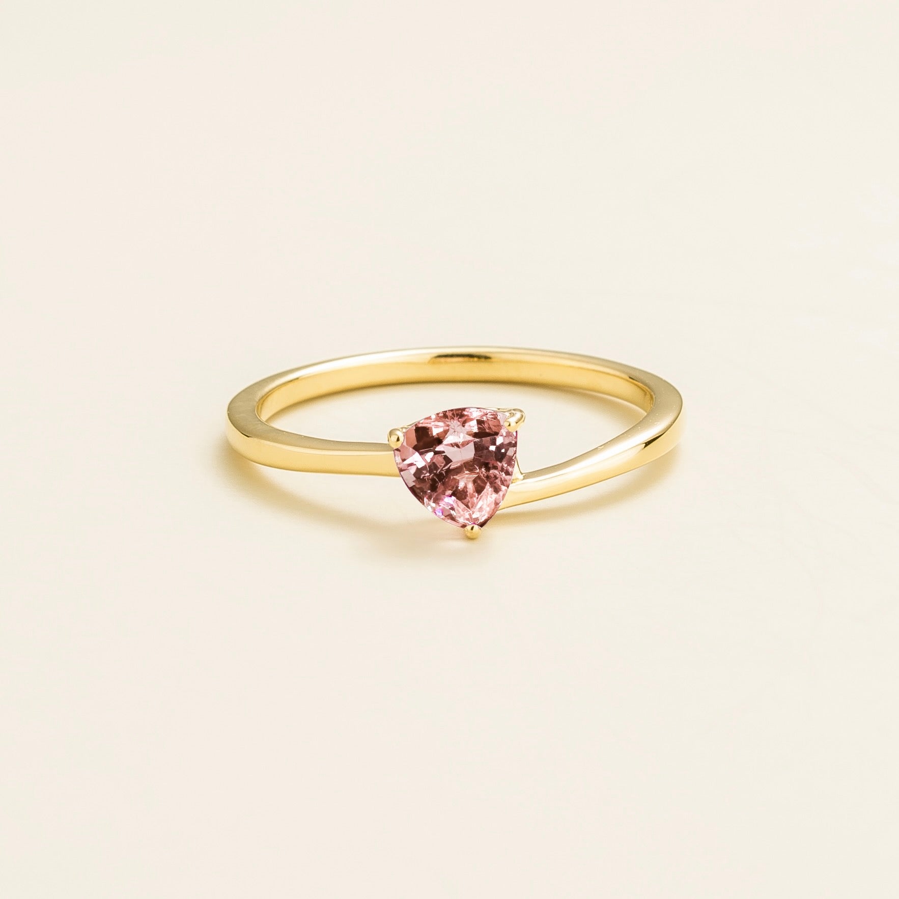 A solitaire gold ring with a trillion-cut morganite centerpiece, displayed against a white background