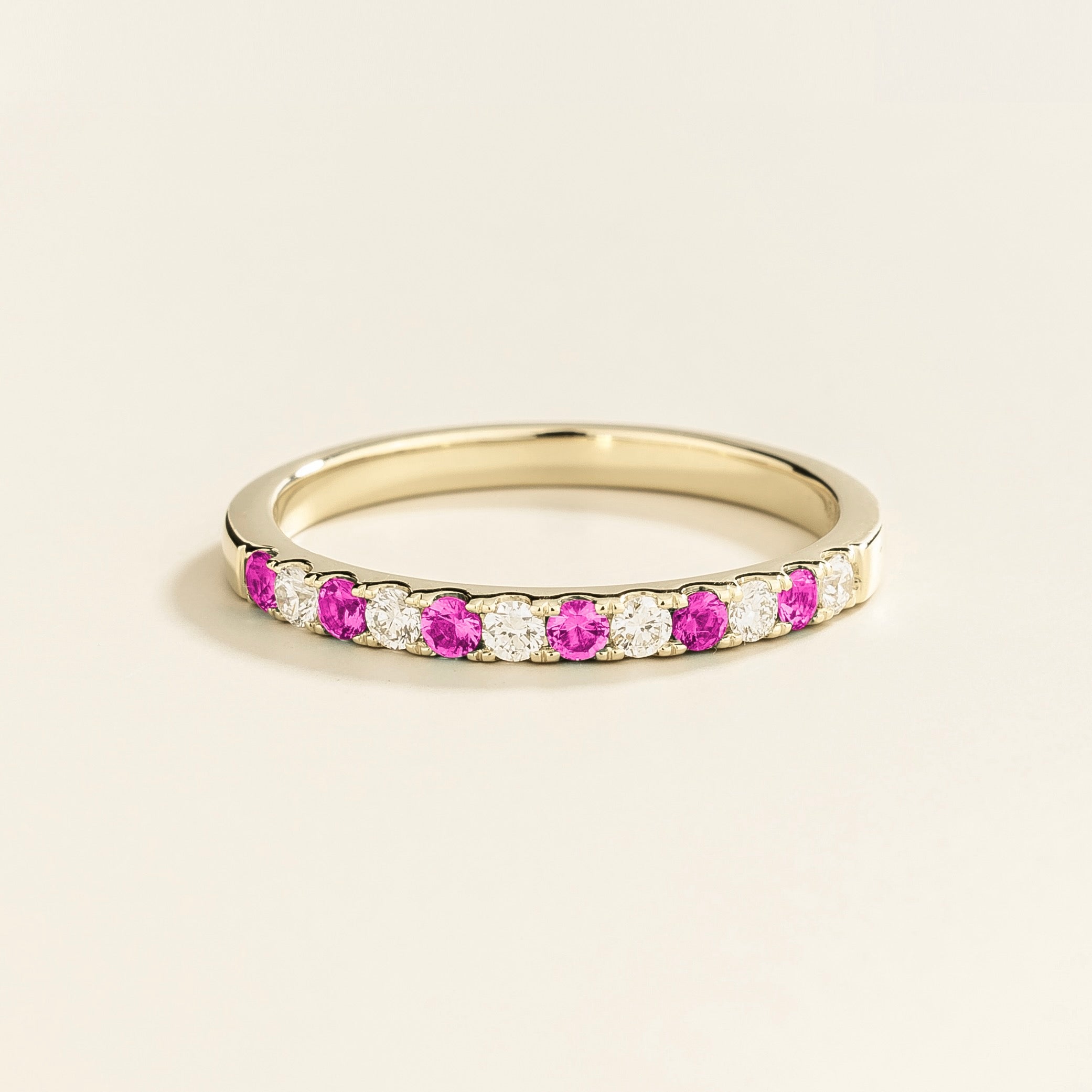 A white gold ring with alternating vivid pink sapphire and diamond elements, creating a half eternity band design.