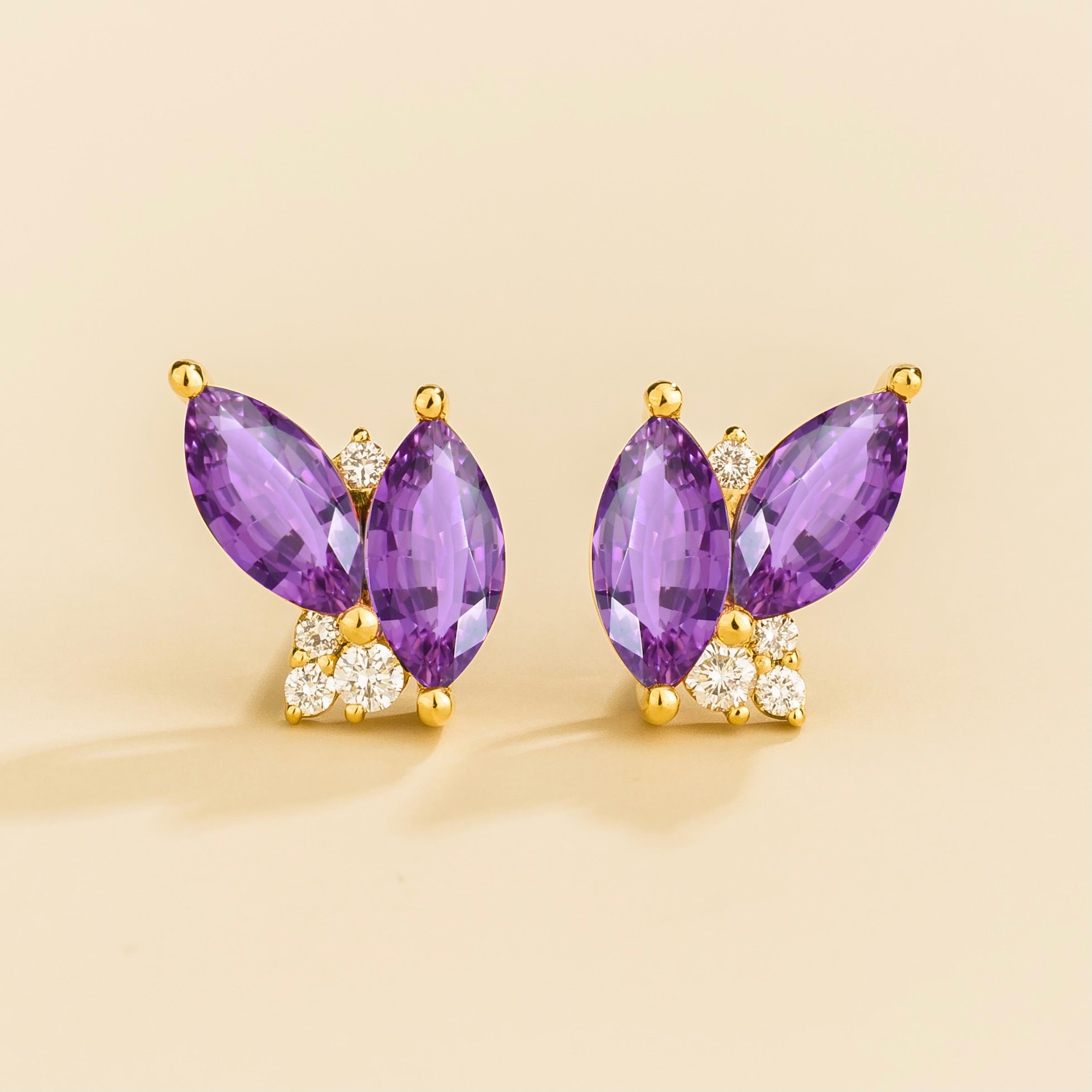A pair of gold earrings featuring marquis purple sapphires and small round diamonds, with a butterfly-like shape.